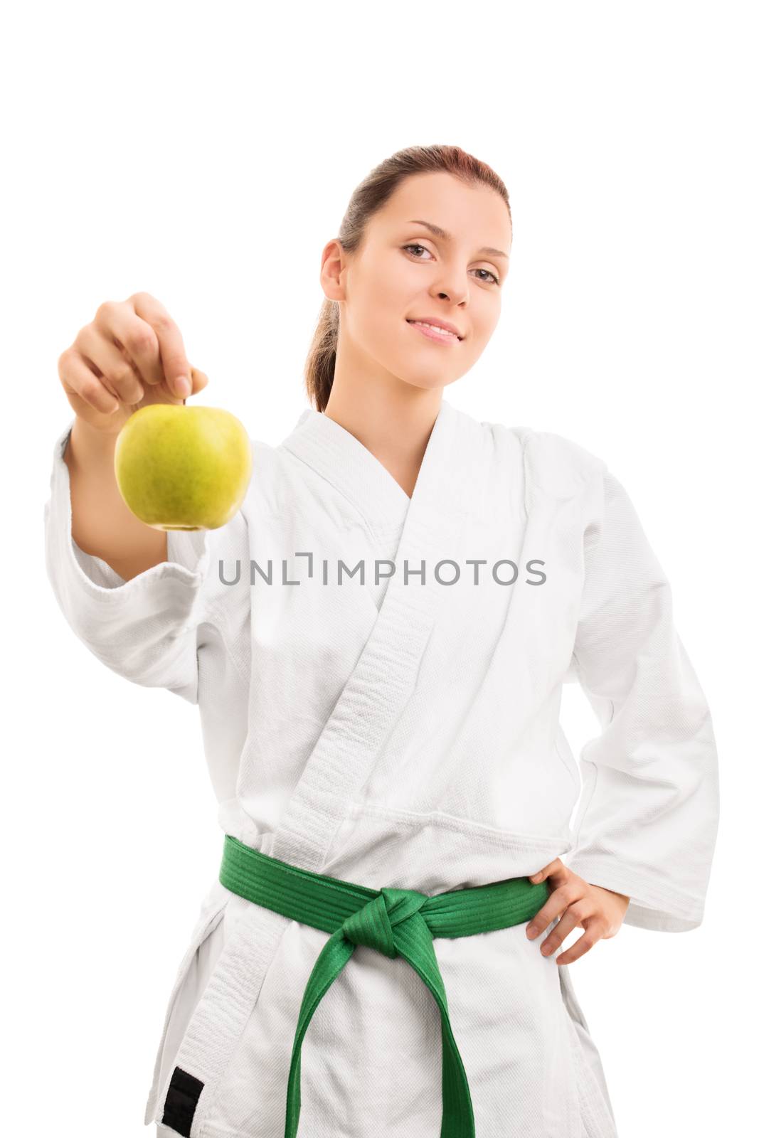 Sports and healthy eating. Beautiful smiling young girl in kimono with green belt offering an apple, isolated on white background.
