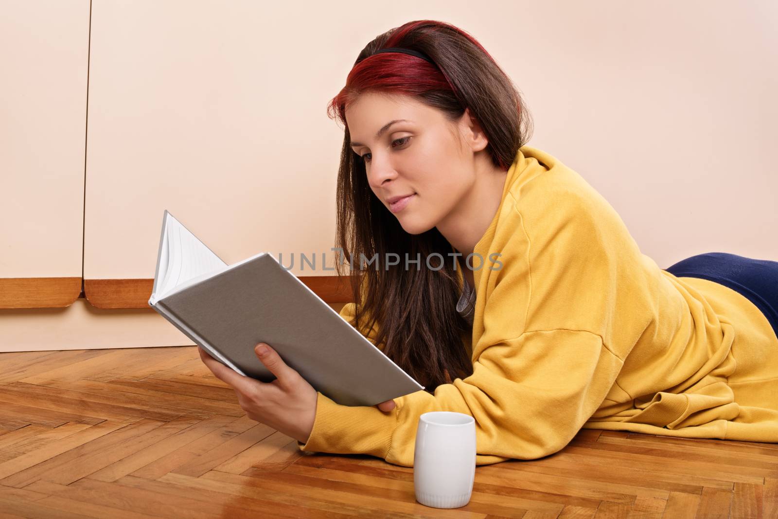 Young girl lying on the floor reading a book by Mendelex
