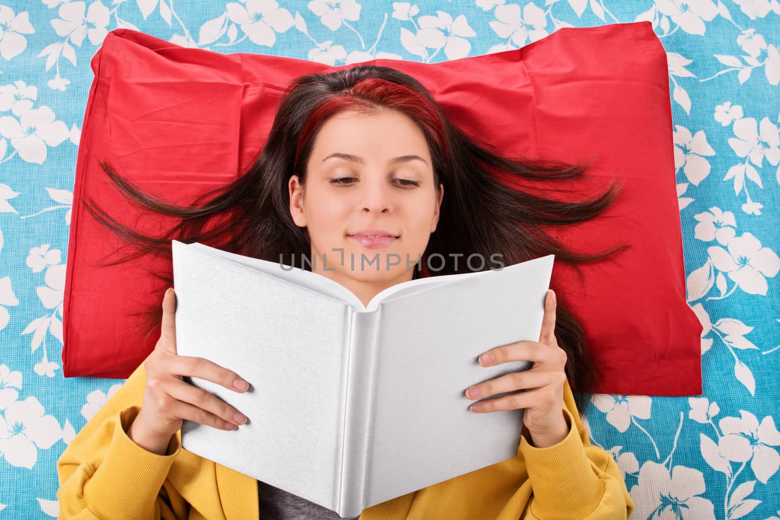 Young girl reading a book on her bed by Mendelex