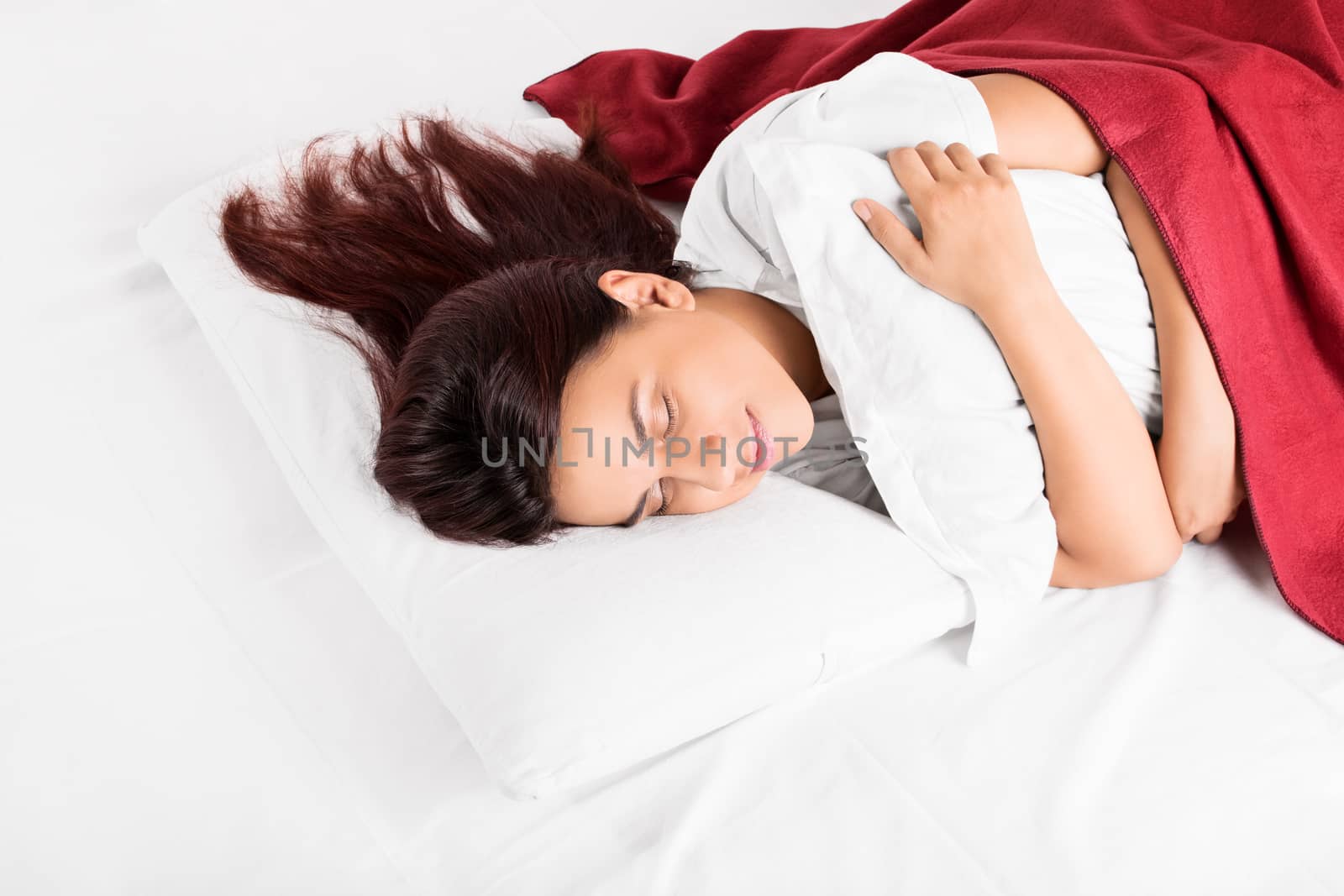 Beautiful young girl comfortably sleeping in bed hugging a pillow.