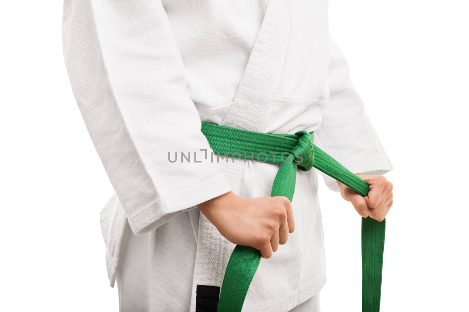 Preparing for training. Close up shot of the mid section of a girl in kimono, tying her green belt, isolated on white background.