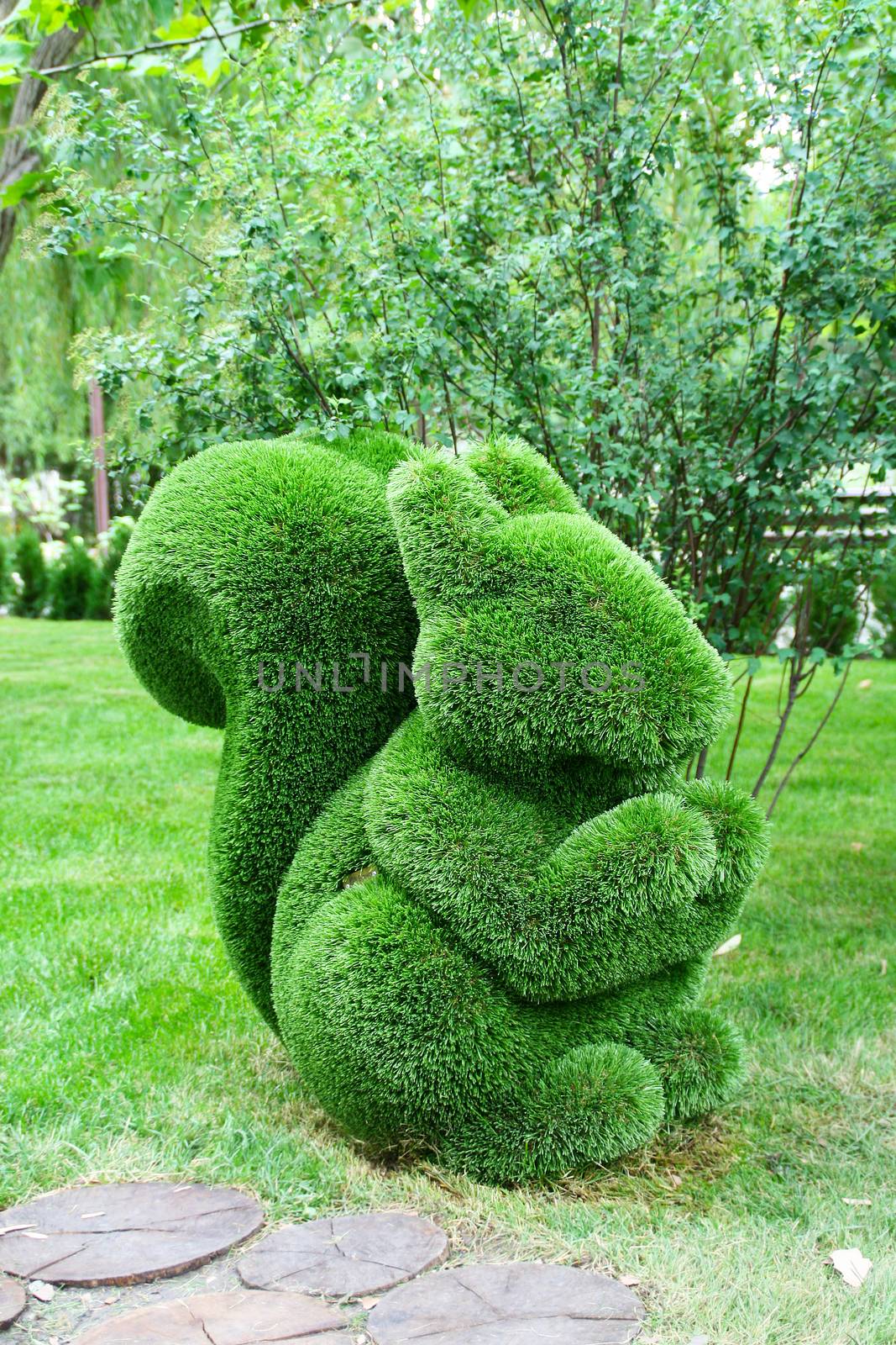 Pictures green squirrel made of artificial grass green against the background of trees.