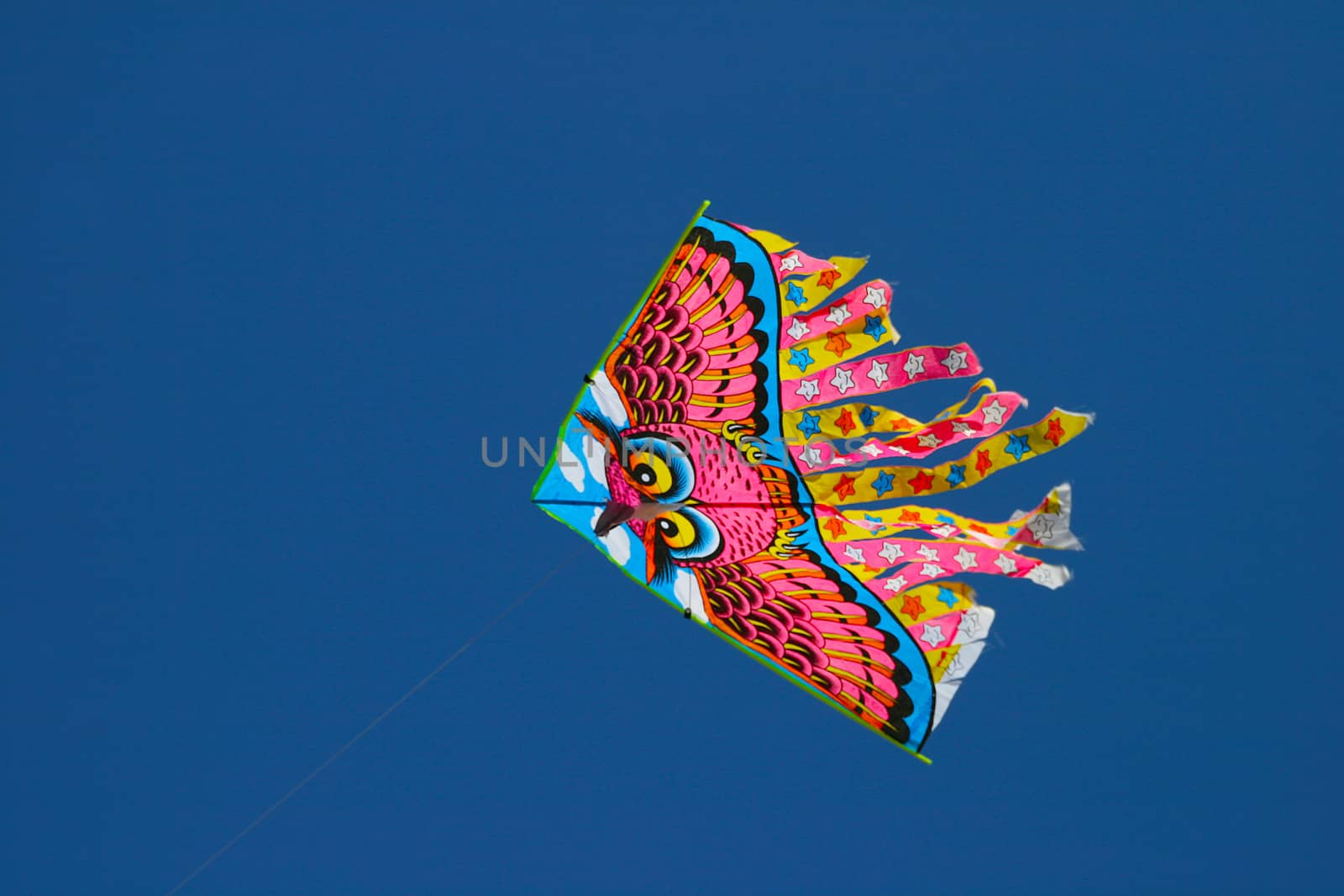 A kite with stripes of red high above the ground in a clear blue sky.