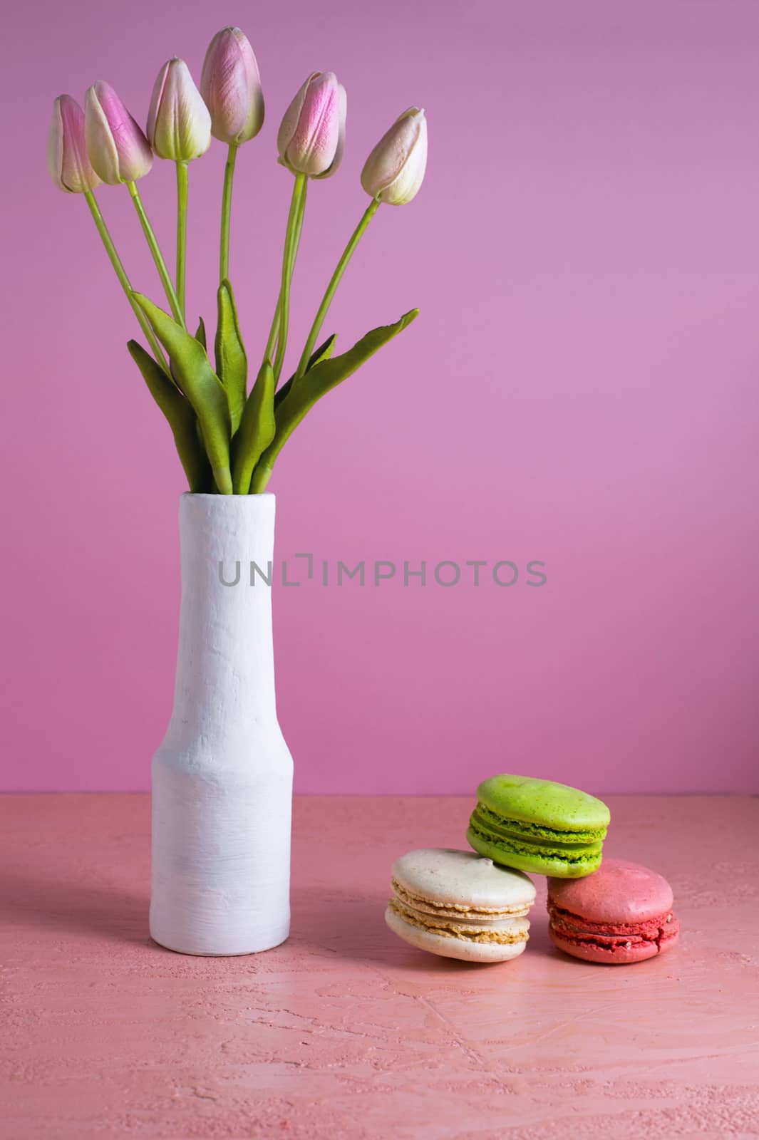 Macaroons on a pale pink background next to a vase of tulips. Place for text