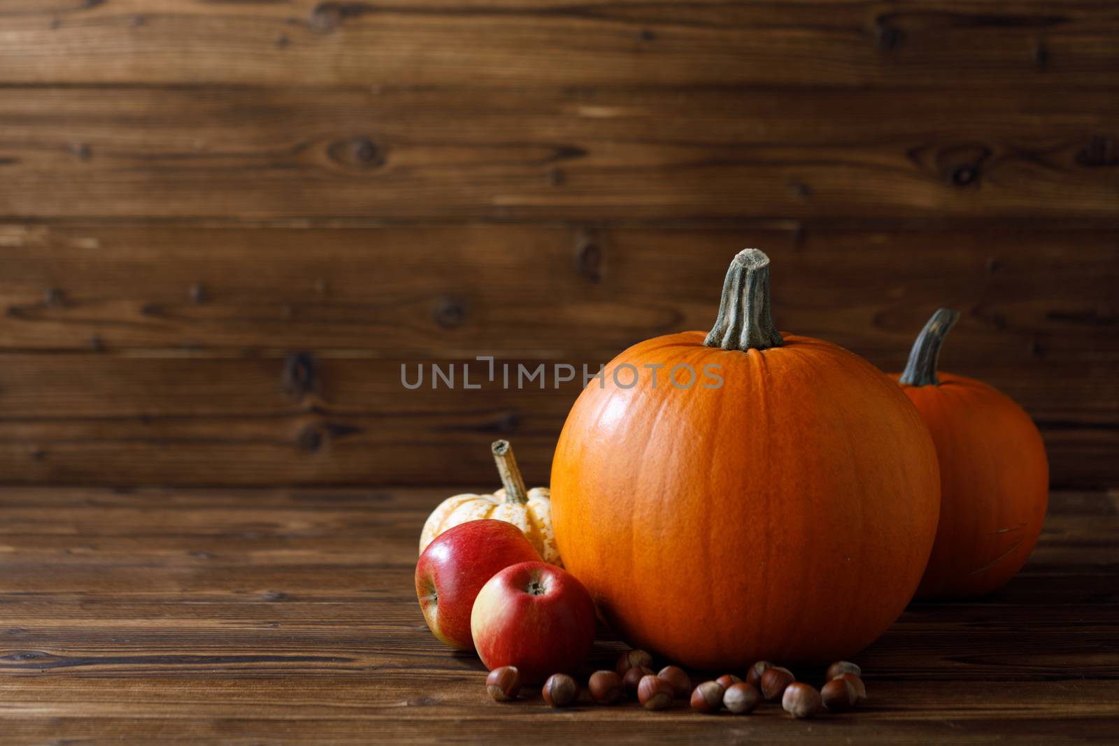 Autumn harvest still life with pumpkins , apples , hazelnuts on wooden background