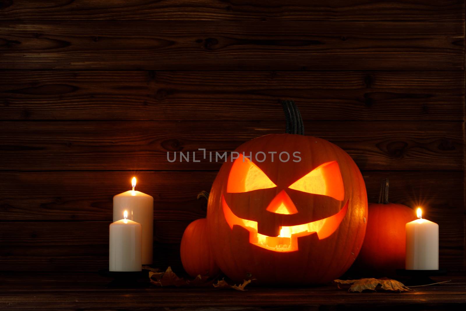 Halloween pumpkin head jack o lantern candles and dry maple leaves on wooden background