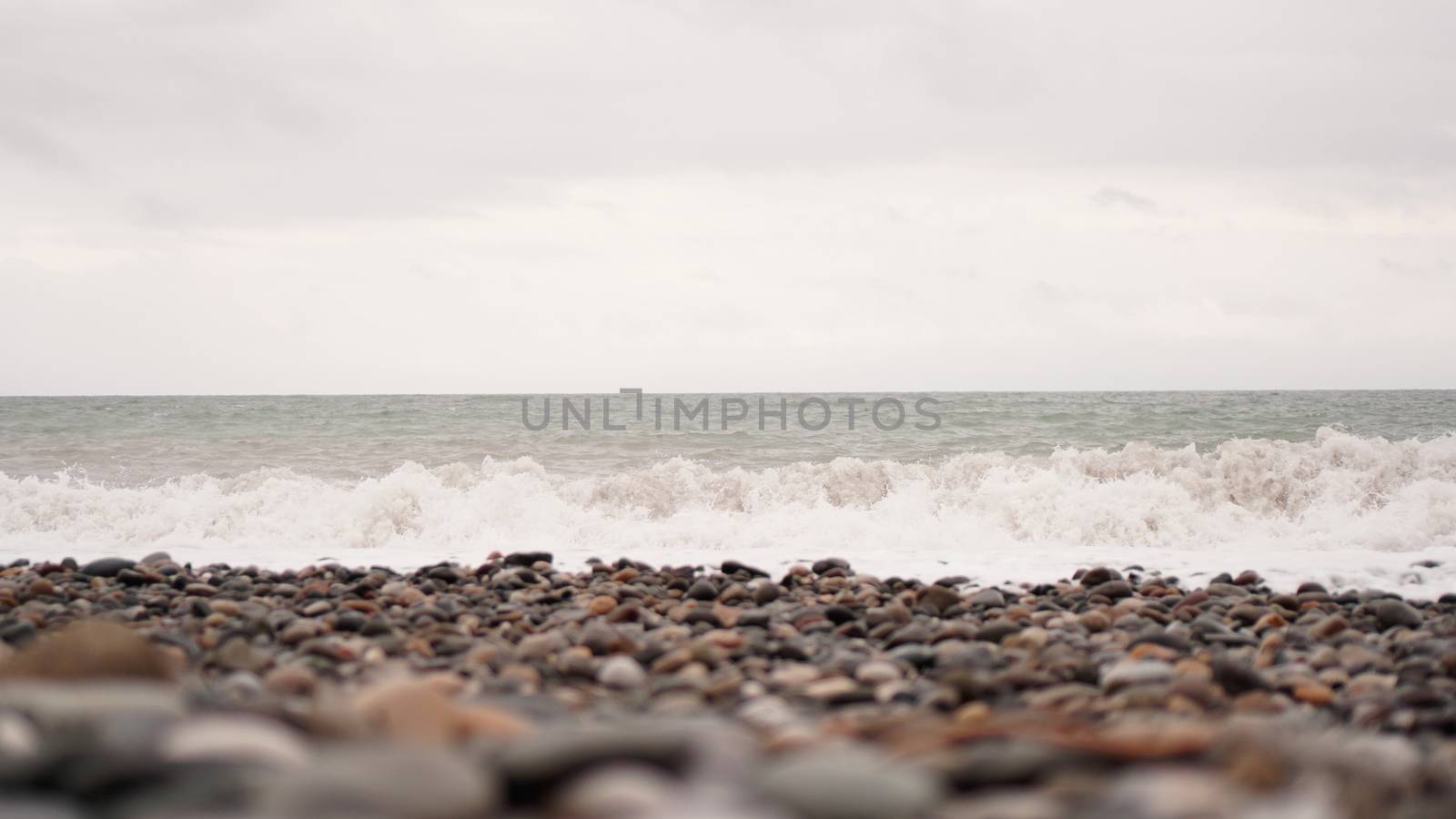 Pebble stones on the shore close up in the blurry light in the distance by natali_brill