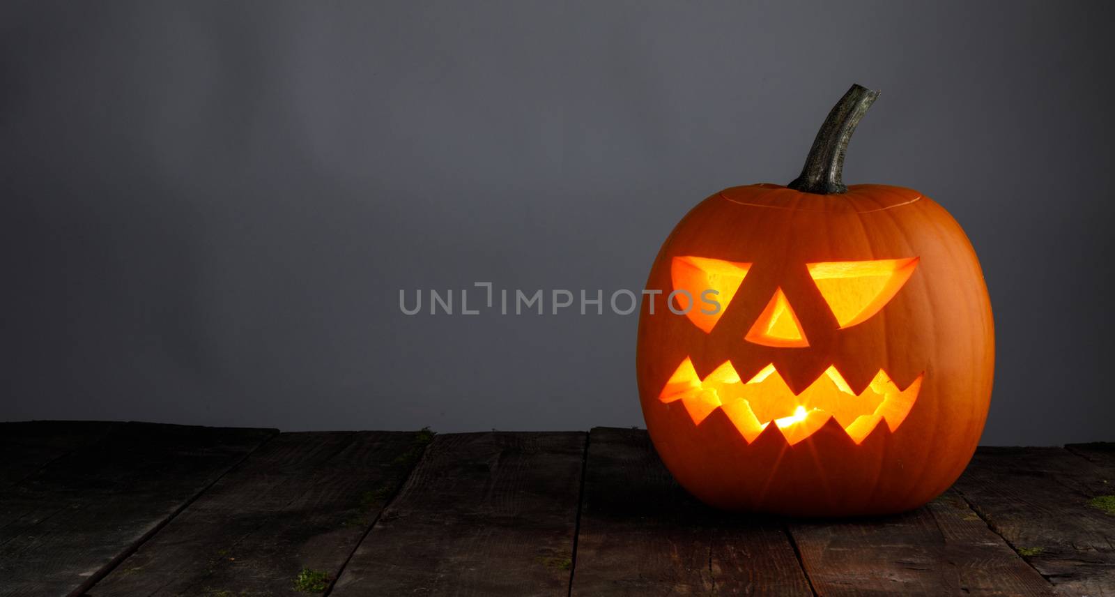 Glowing Halloween pumpkin head jack lantern on gray old wooden background