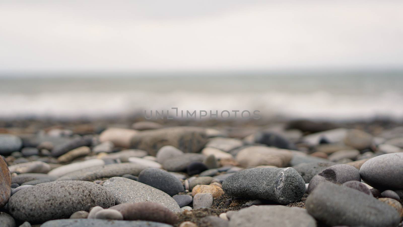 Pebble stones on the shore close up in the blurry light in the distance background.