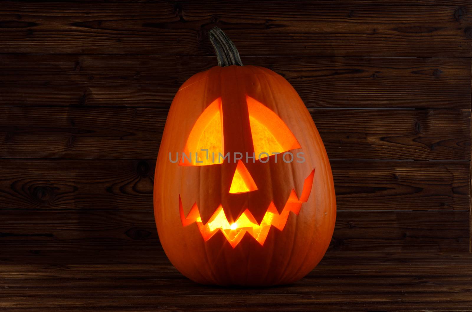 Halloween pumpkin head jack o lantern with candle inside on wooden background