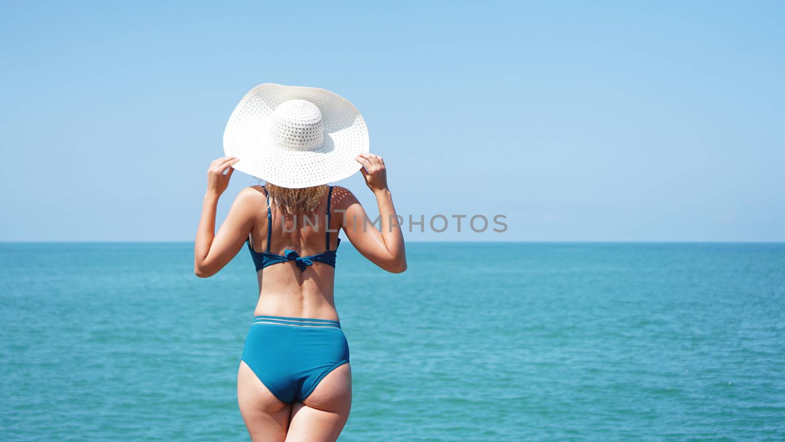 Young woman standing on sand near sea and holding a hat by natali_brill