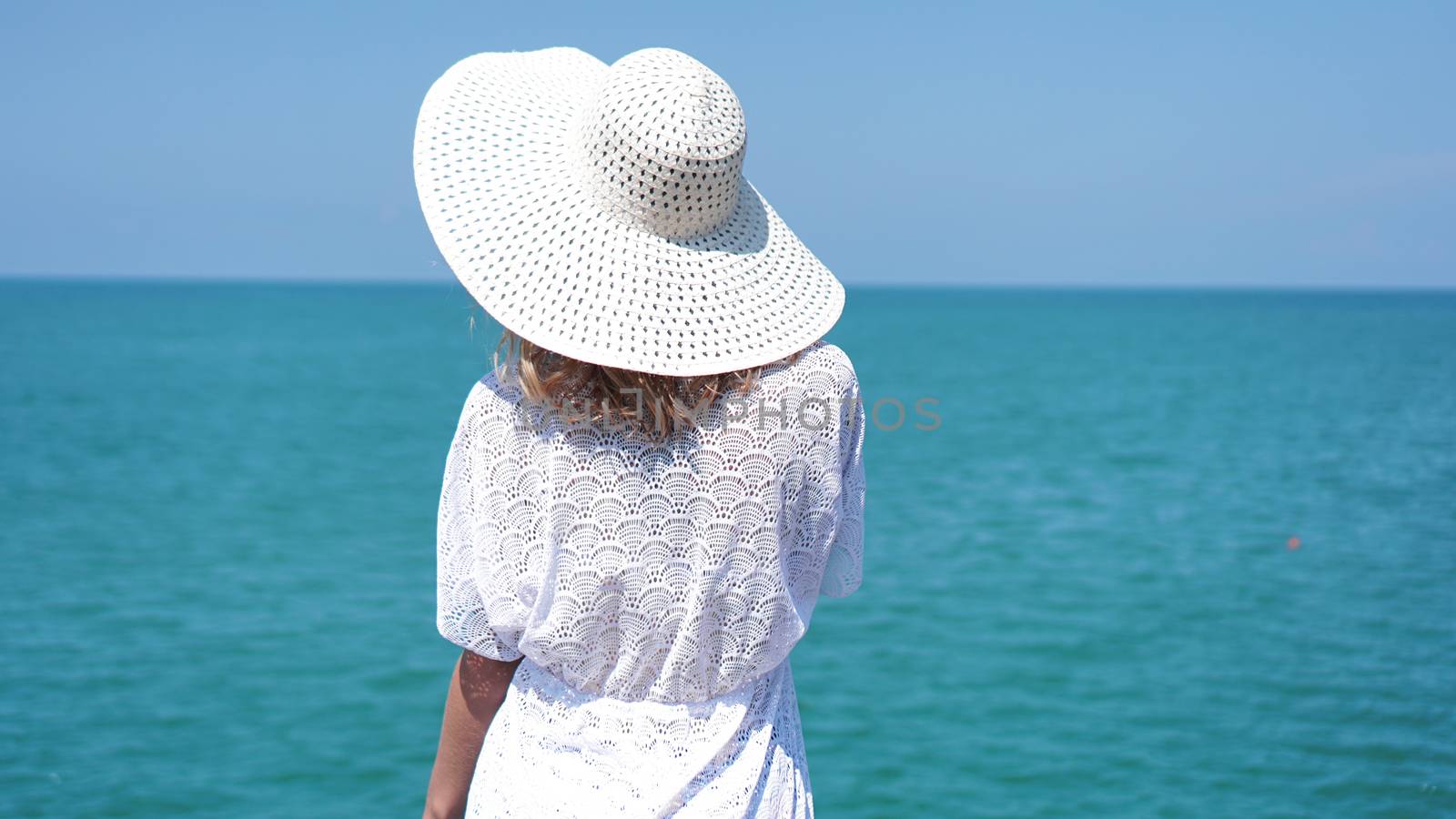 Young woman standing on sand near sea and holding a white hat