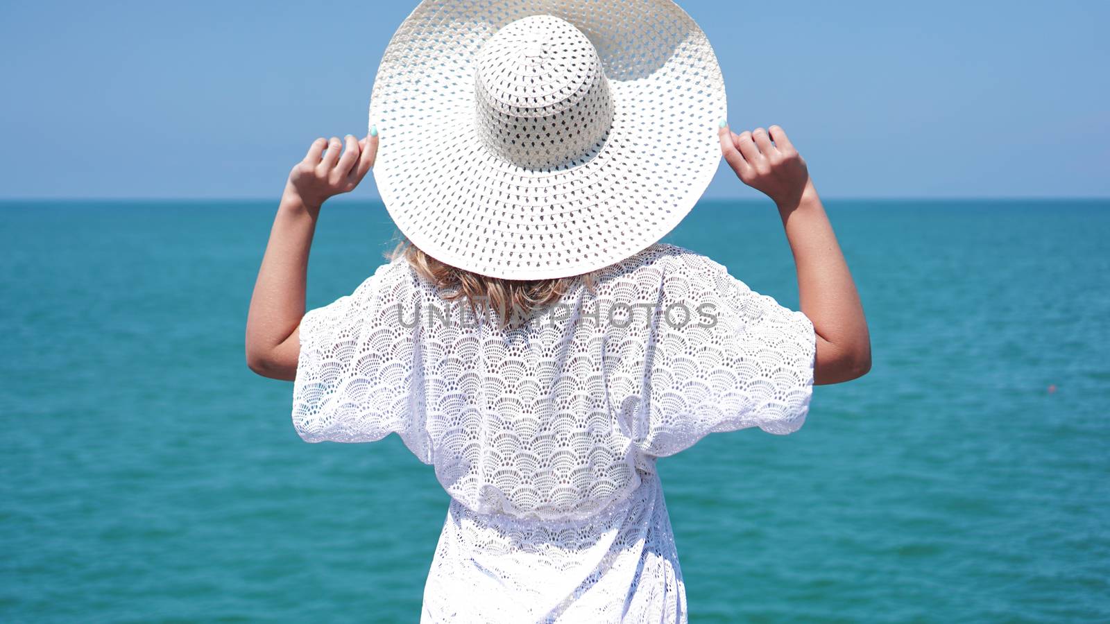 Young woman standing on sand near sea and holding a white hat