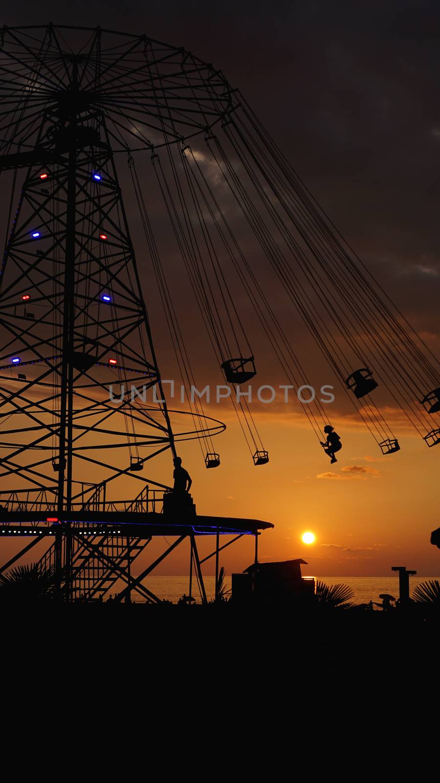 Swinging carousel roundabout chain ride at sunset. Entertainment on the beach, silhouettes of palm trees on a background of sea sunset