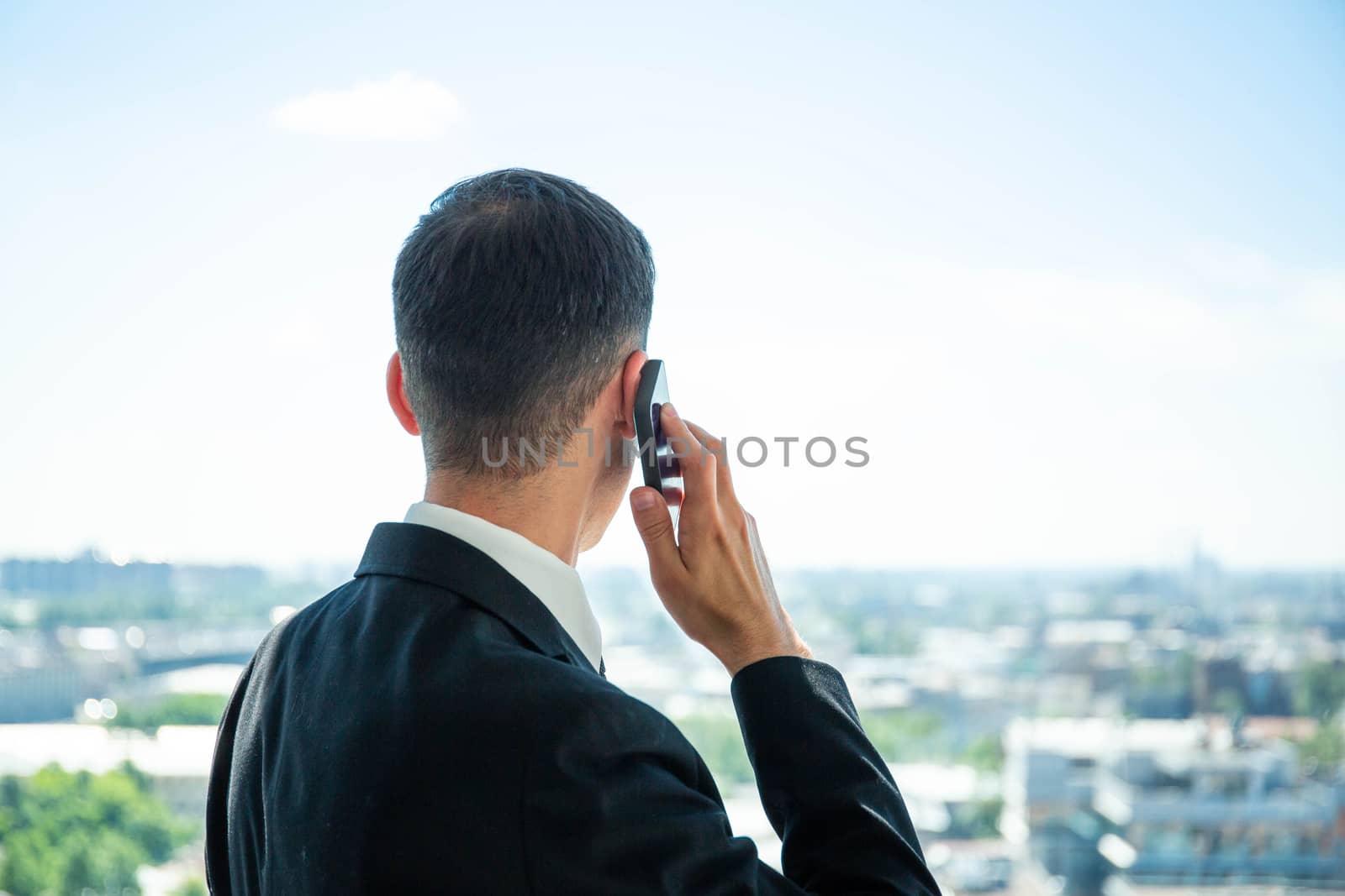 Stylish business man in the background of a large window calling by phone