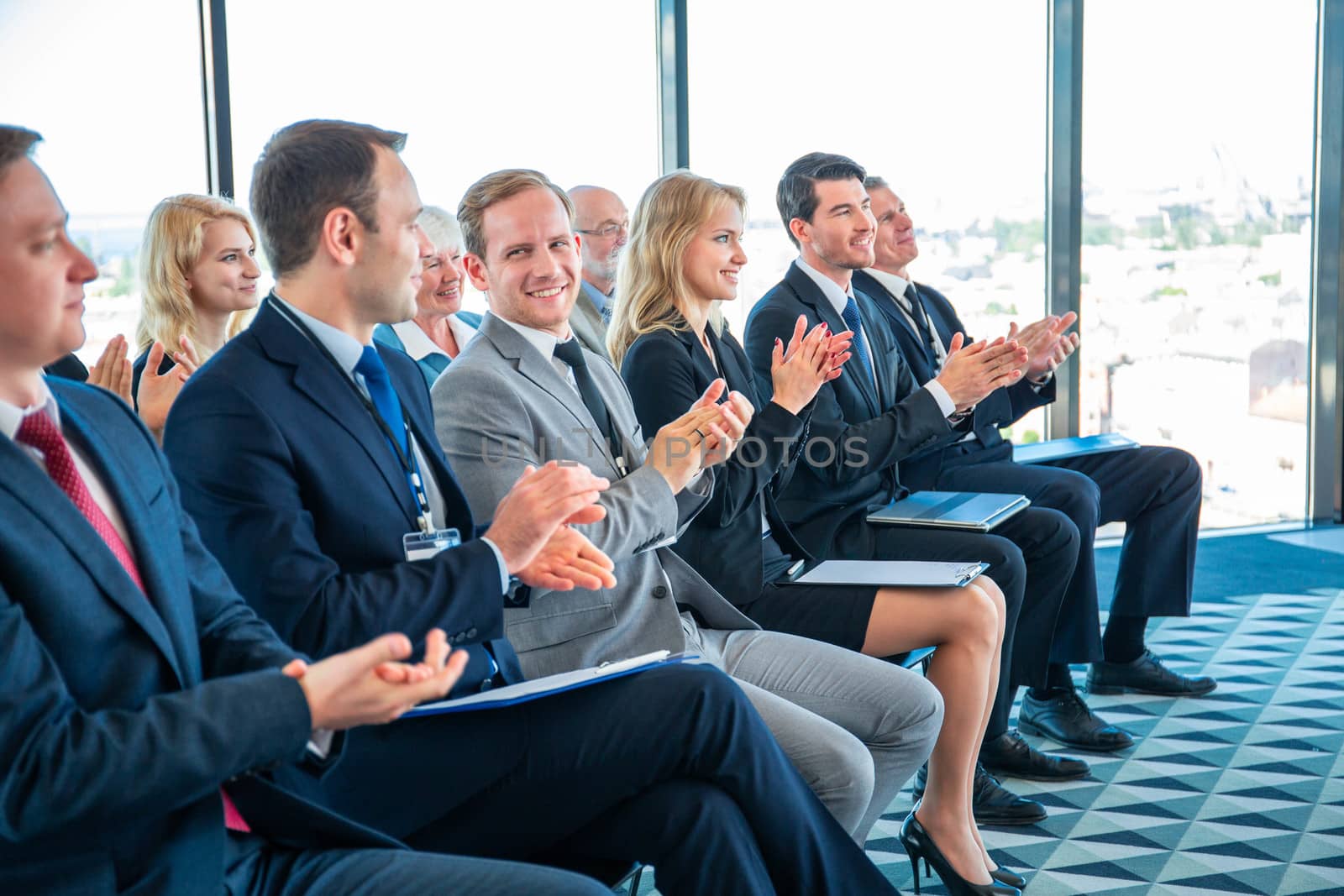 Audience of happy business people sitting at training room, conference hall, applauding to speaker