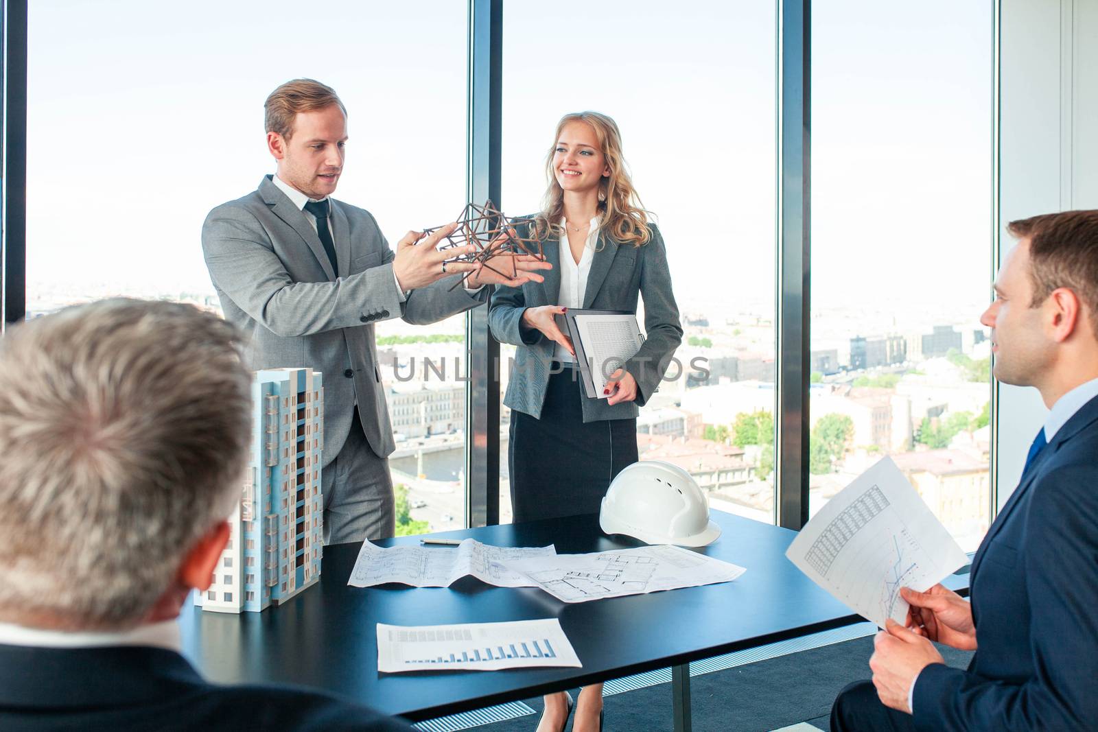 Business meeting of architects and investors discussing new construction shapes at presentation, model of modern multi storey residential building house on table