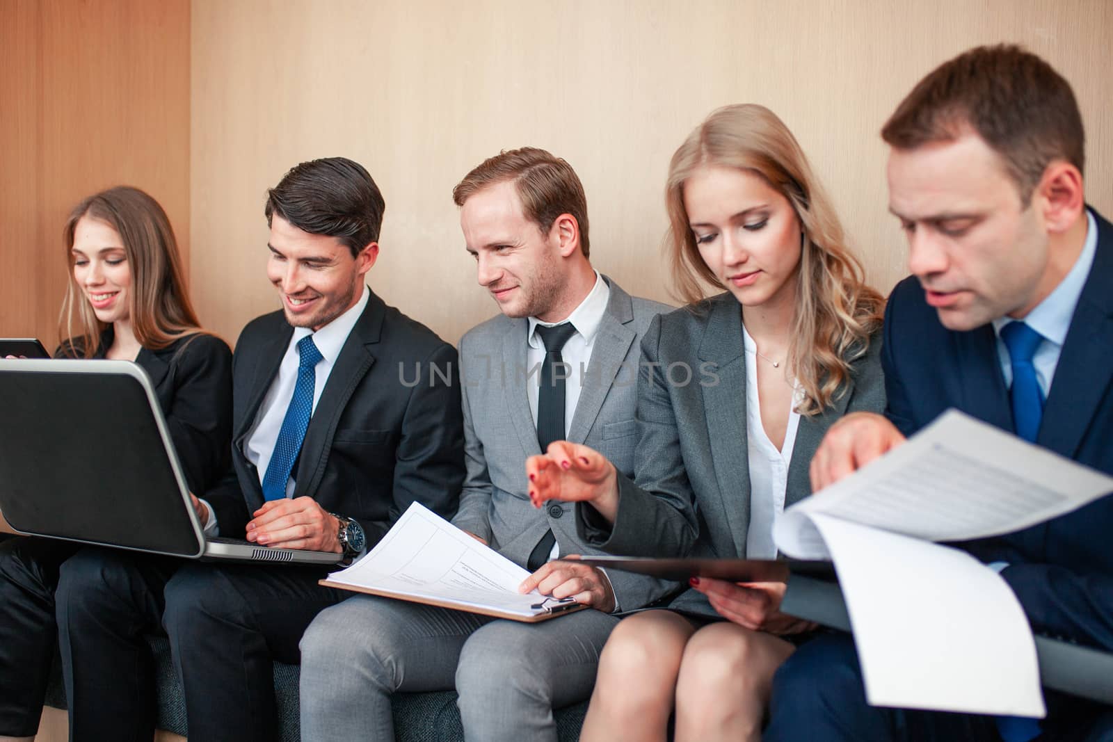 Business people working together sitting in a row in lobby and holding laptop and documents on knees