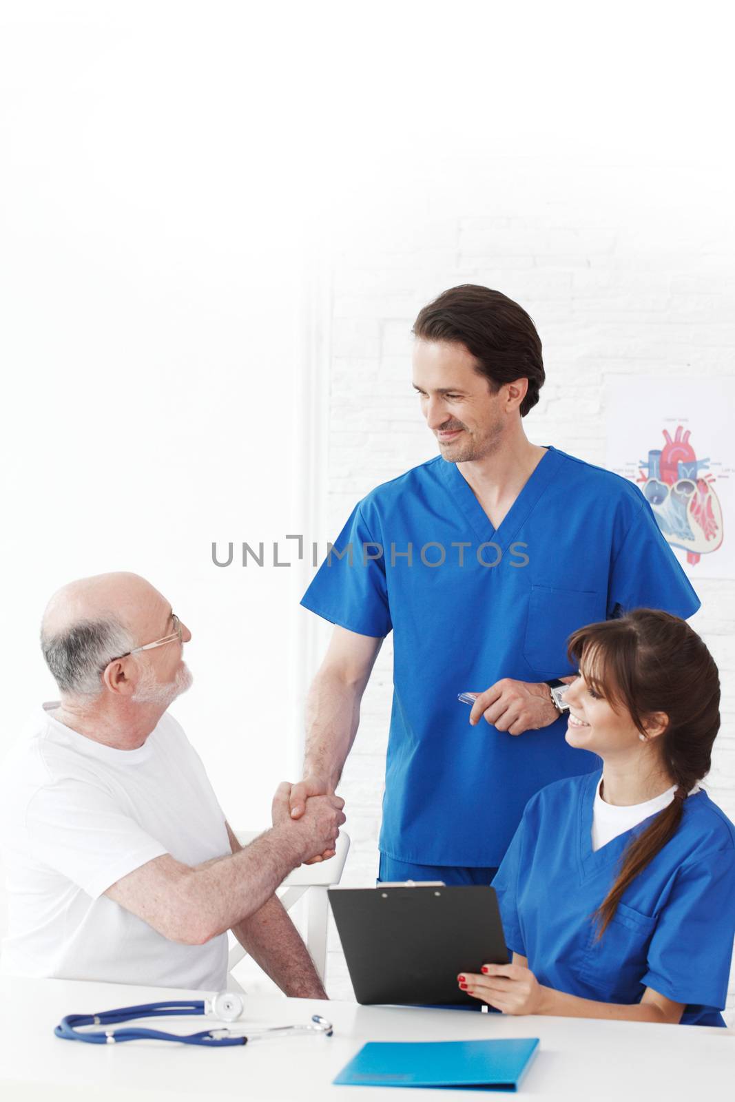 Happy senior patient and doctors in hospital shaking hands