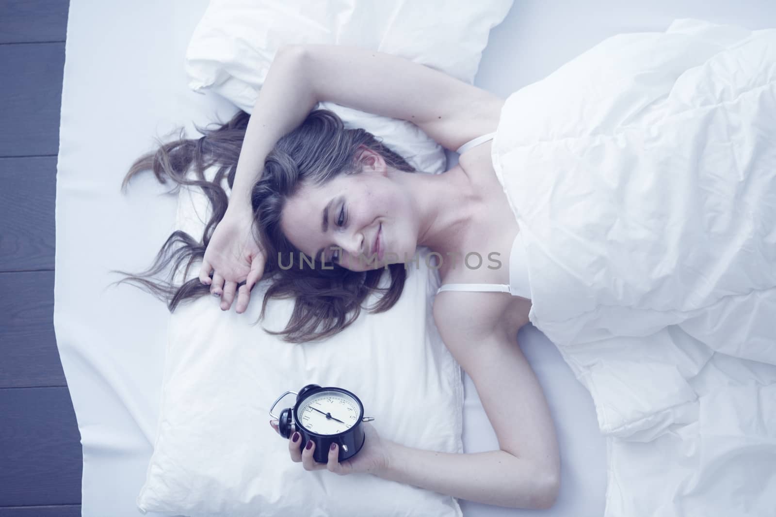 Young beautiful girl waking up with alarm clock