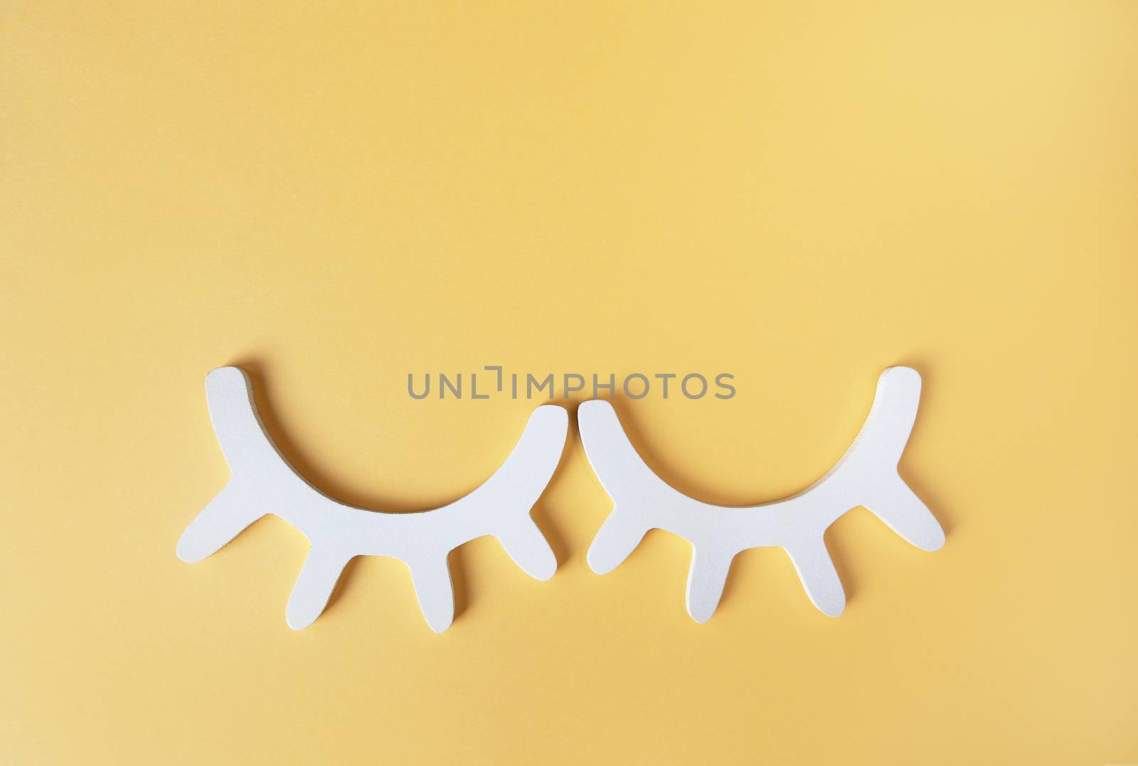 White wooden closed eyes with eyelashes on pastel yellow background. Stylish wall decor. Top view, flat lay. Concept of vivid sweet dreams. Accessories for kids room. Minimal style.