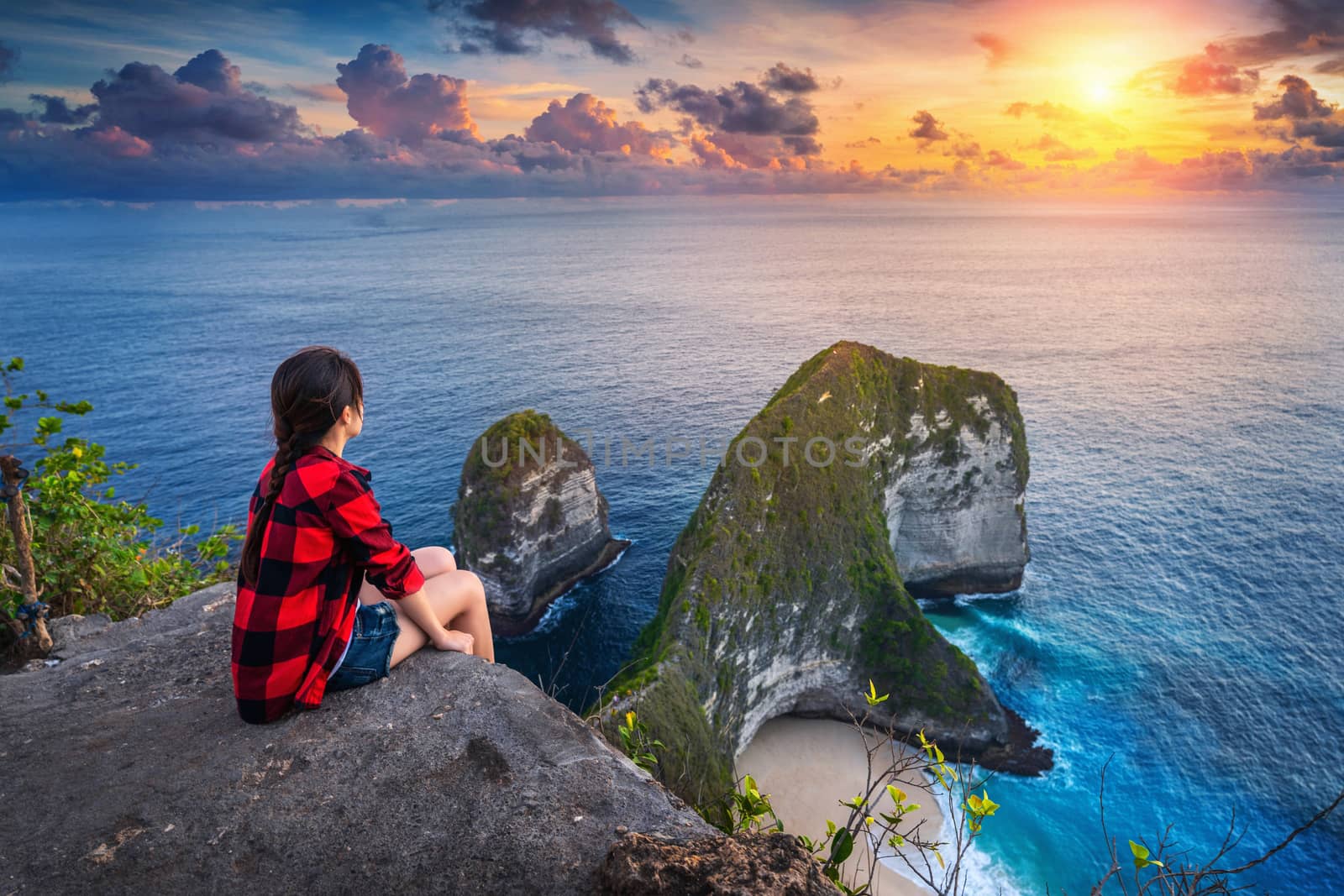 Woman sitting on cliff and looking at sunset at Kelingking Beach in Nusa penida island, Bali, Indonesia. by gutarphotoghaphy