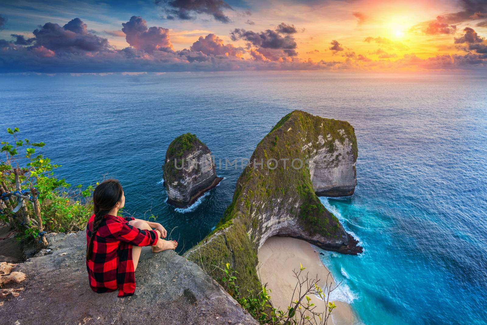 Woman sitting on cliff and looking at sunset at Kelingking Beach in Nusa penida island, Bali, Indonesia. by gutarphotoghaphy