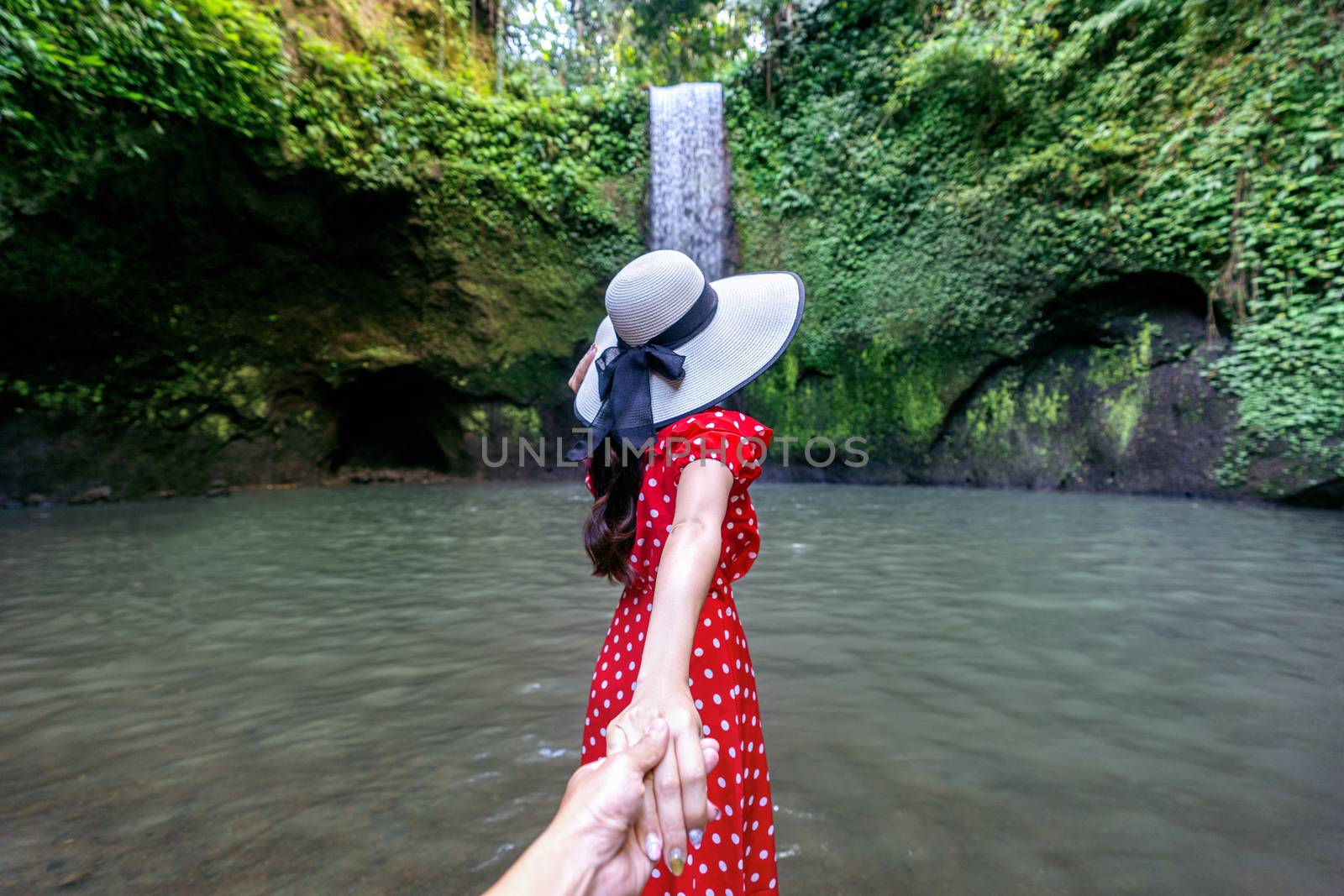 Women tourists holding man's hand and leading him to Tibumana waterfall in Bali, Indonesia.