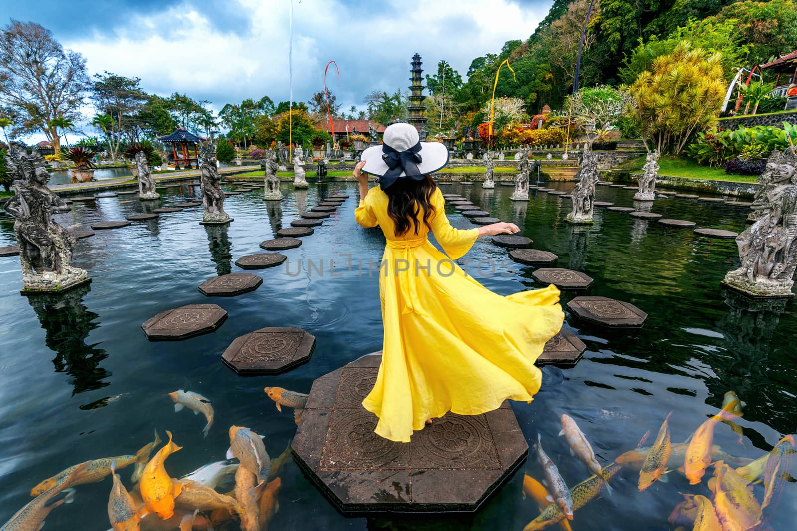 Woman standing in pond with colorful fish at Tirta Gangga Water Palace in Bali, Indonesia. by gutarphotoghaphy