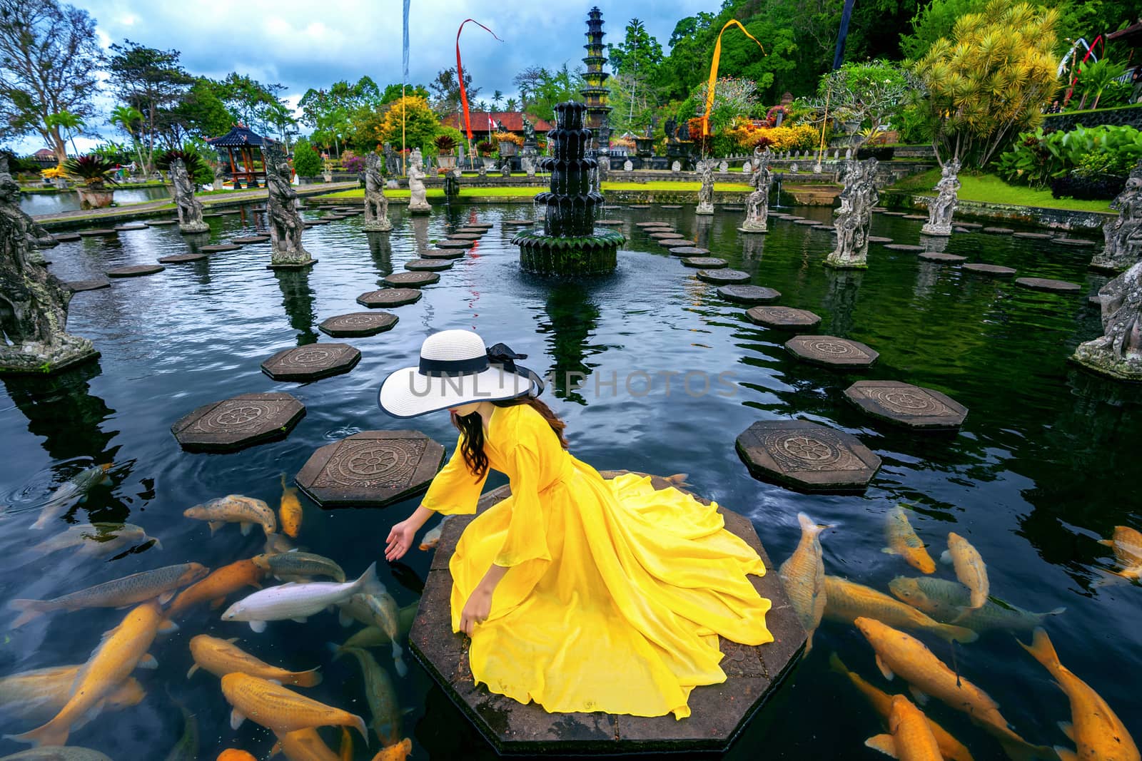 Woman feeding colorful fish in pond at Tirta Gangga Water Palace in Bali, Indonesia. by gutarphotoghaphy