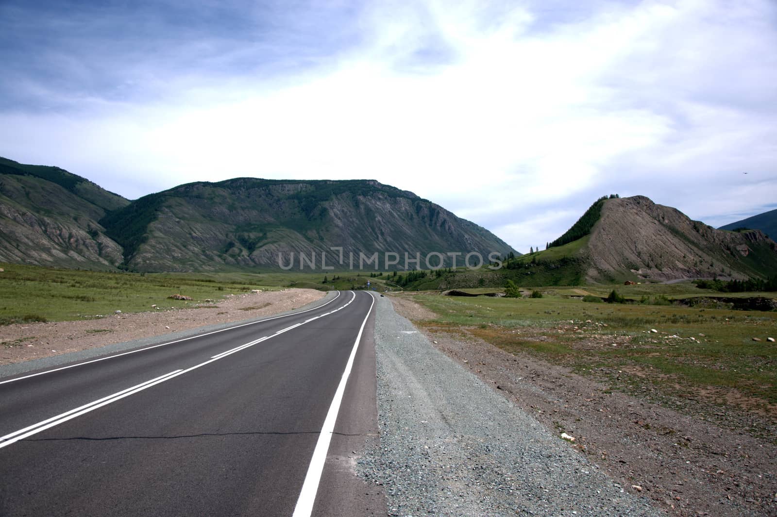 A direct asphalt road running through a valley surrounded by mountains. Altai, Siberia, Russia.