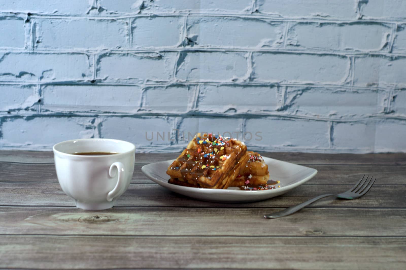 Breakfast, a fork, a cup of black coffee and a plate with two Viennese waffles are on a wooden table. Close-up.