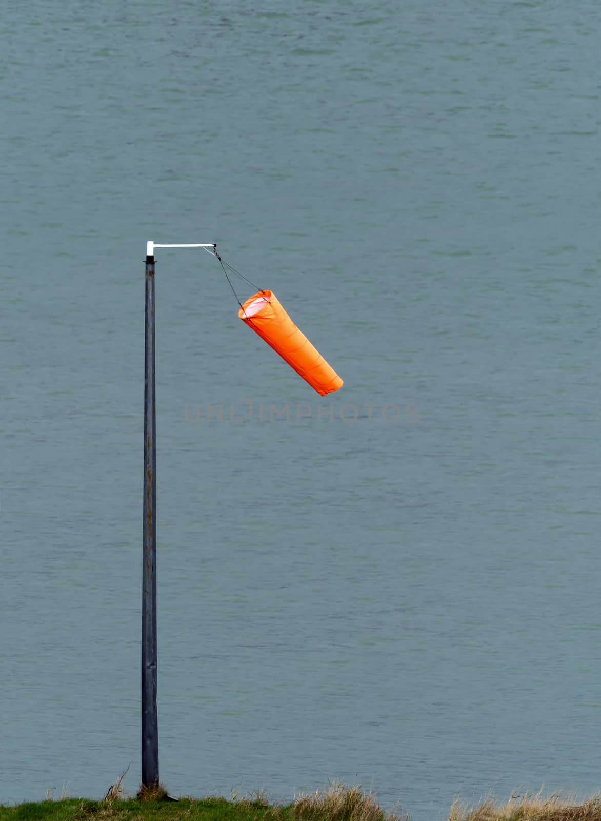 Orange wind sock hanging limply in light wind by Sussex harbour.
