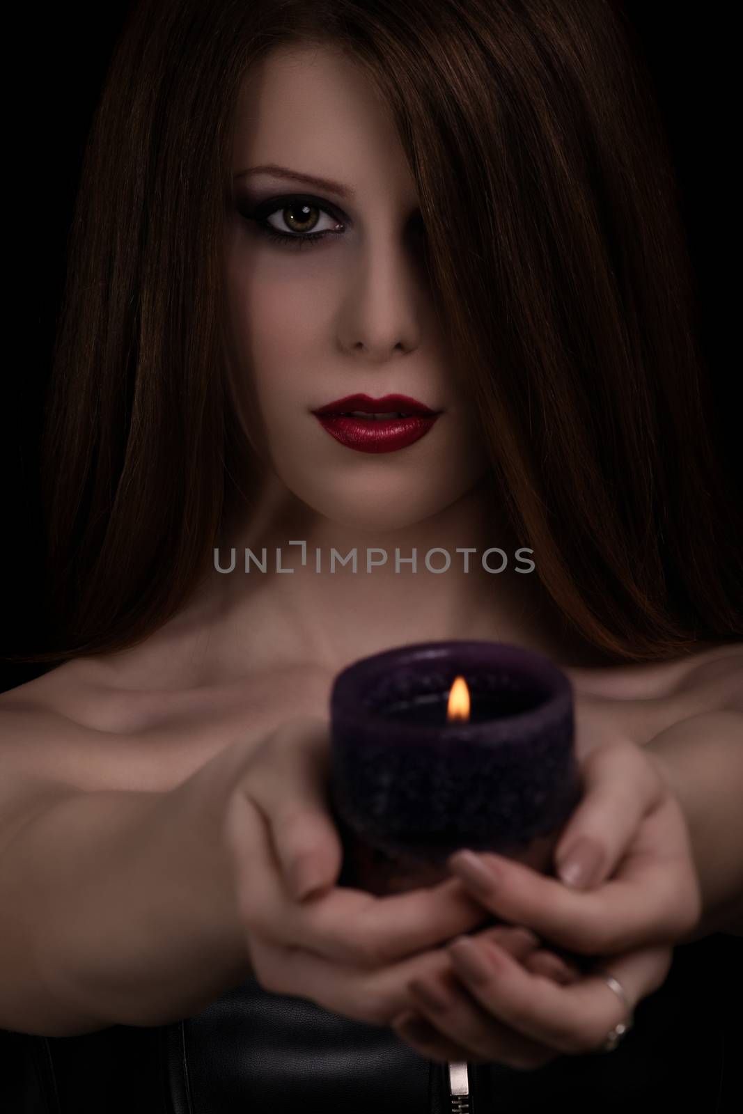 Low key portrait of a mystical beautiful goth girl holding a candle, isolated on black background.