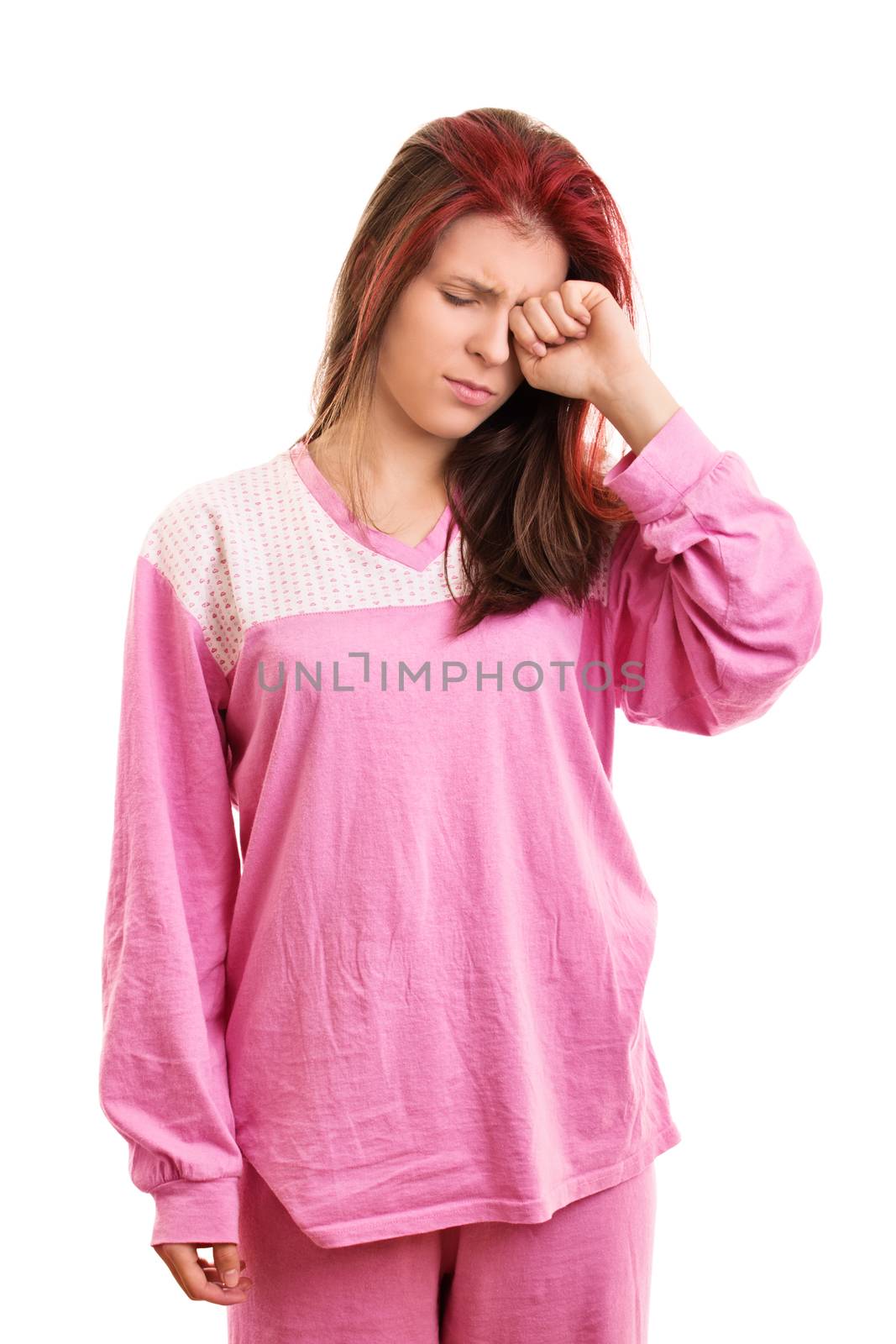 Leave me alone, I'm so sleepy. A portrait of a sleepy beautiful young girl in pink pajamas rubbing her eye, isolated on white background.