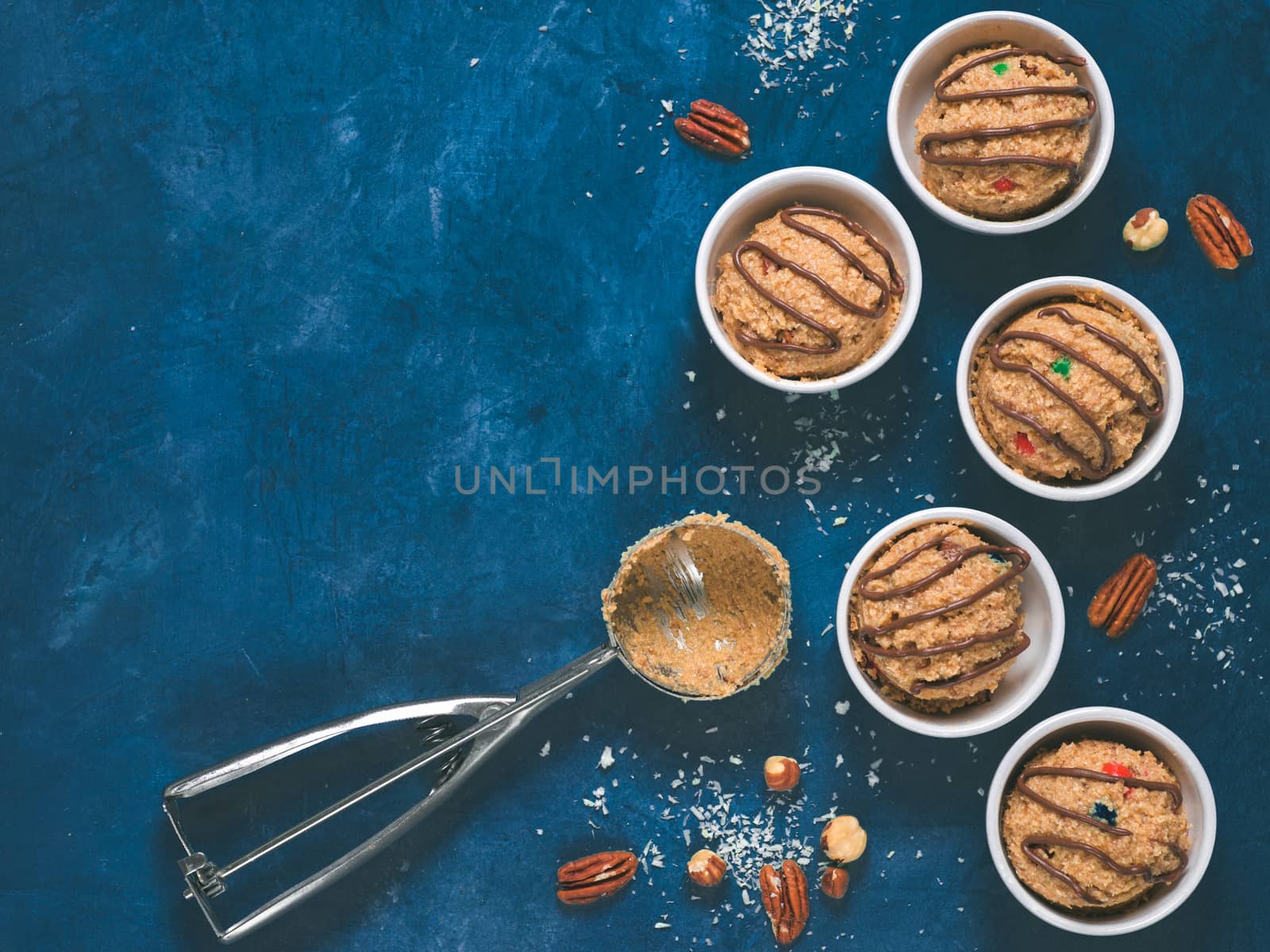 Safe-to-eat raw monster cookie dough in small portion bowl, ice cream scoop and nuts on blue background. Ideas and recipes for kids and toddlers meal. Top view or flat-lay. Copy space for text.