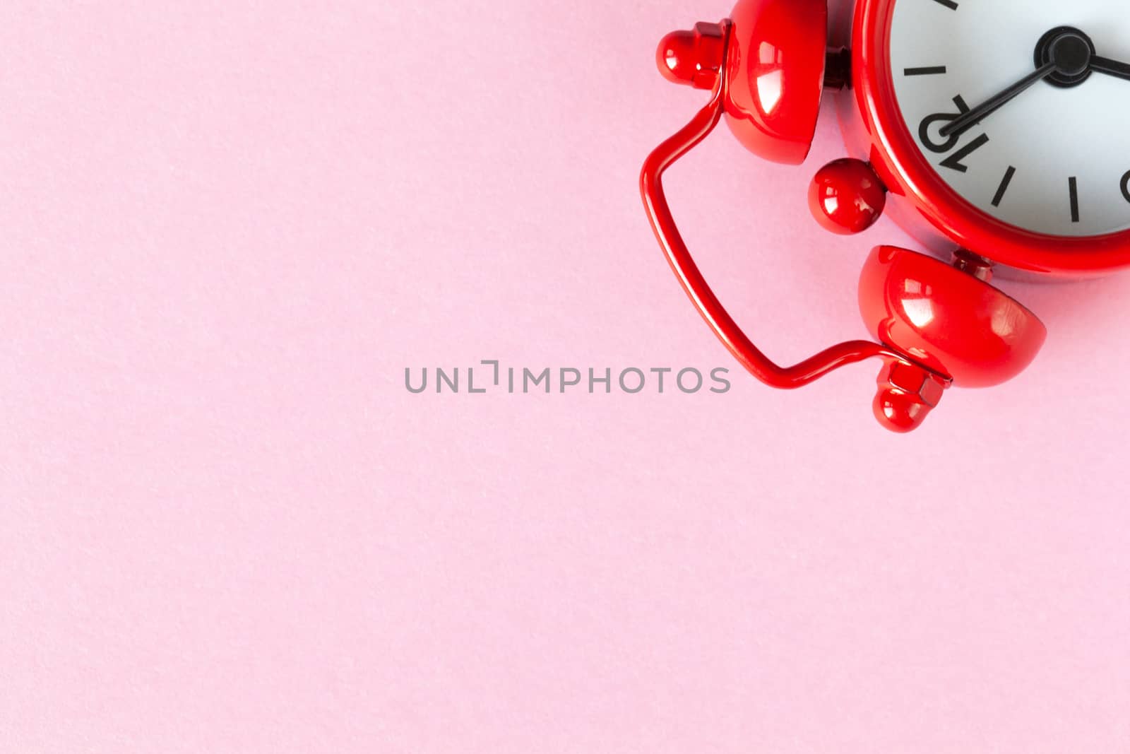 Red small alarm clock on light pastel pink background with copy space, flat lay. Minimal style. Time management concept, free time for important things. One watch is located in upper corner.