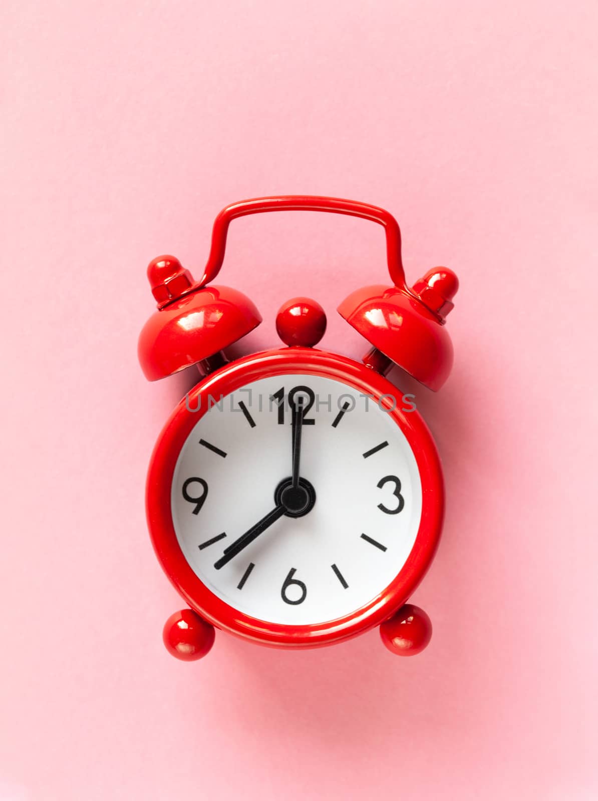 Red small alarm clock on light pastel pink background, flat lay, macro. Minimal style. Time management concept, free time for important things. Vertical. Central composition.