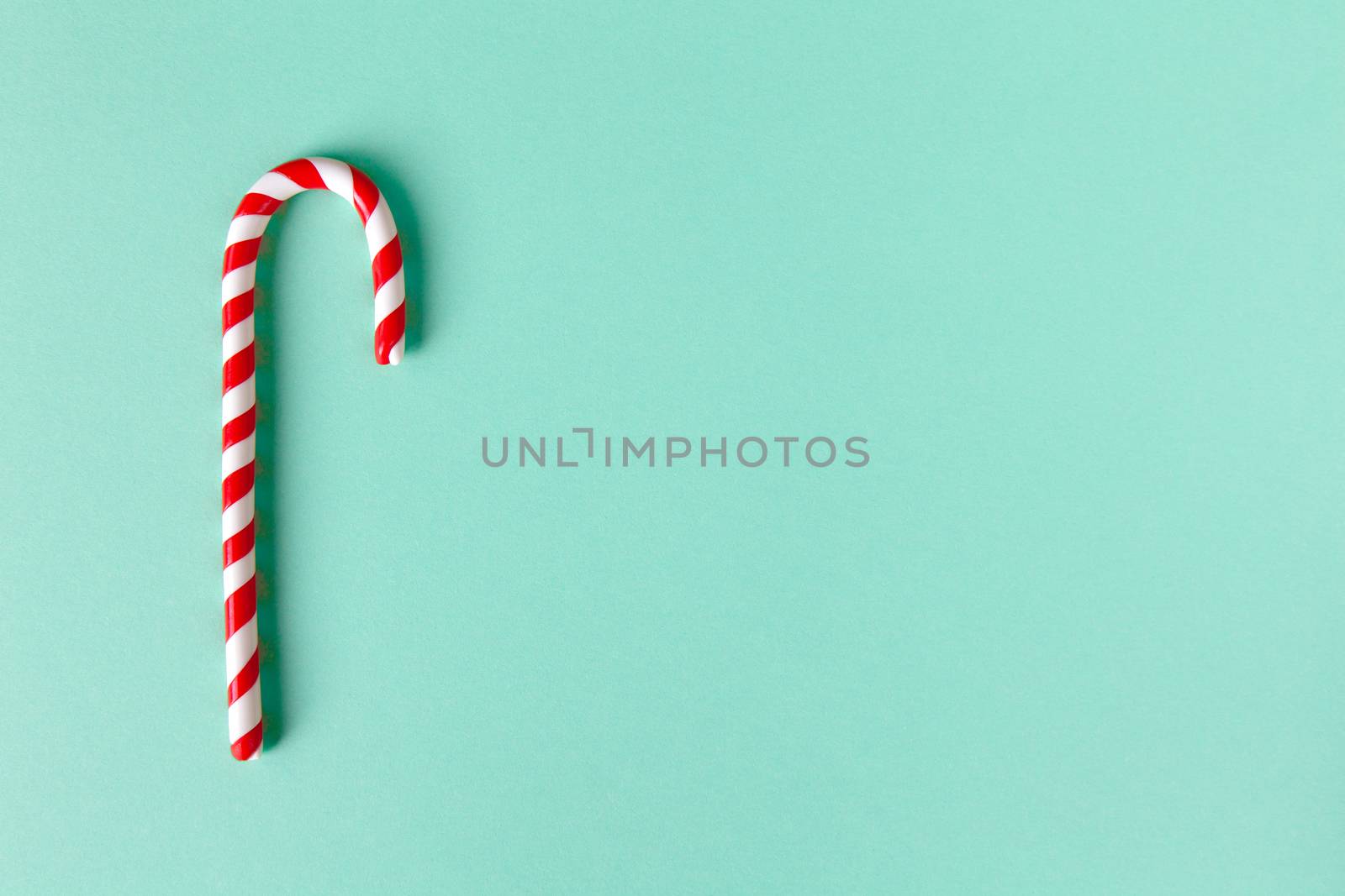 Christmas peppermint candy cane on pastel turquoise background. Festive minimal style flat lay. Mockup with copy space for greeting card, invitation, social media. Horizontal.