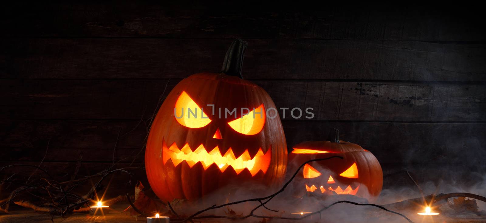 Halloween pumpkins head jack o lantern, candles and dry maple leaves in mist