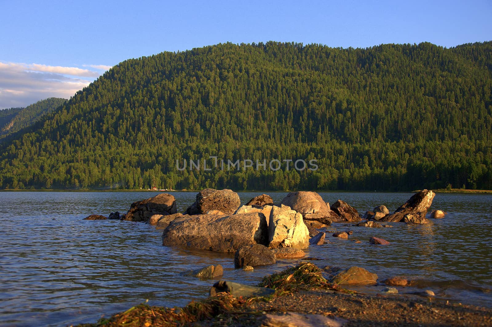 A stone ridge running from the shore to a mountain lake at sunset. Teletskoye Lake, Altai, Siberia, Russia.