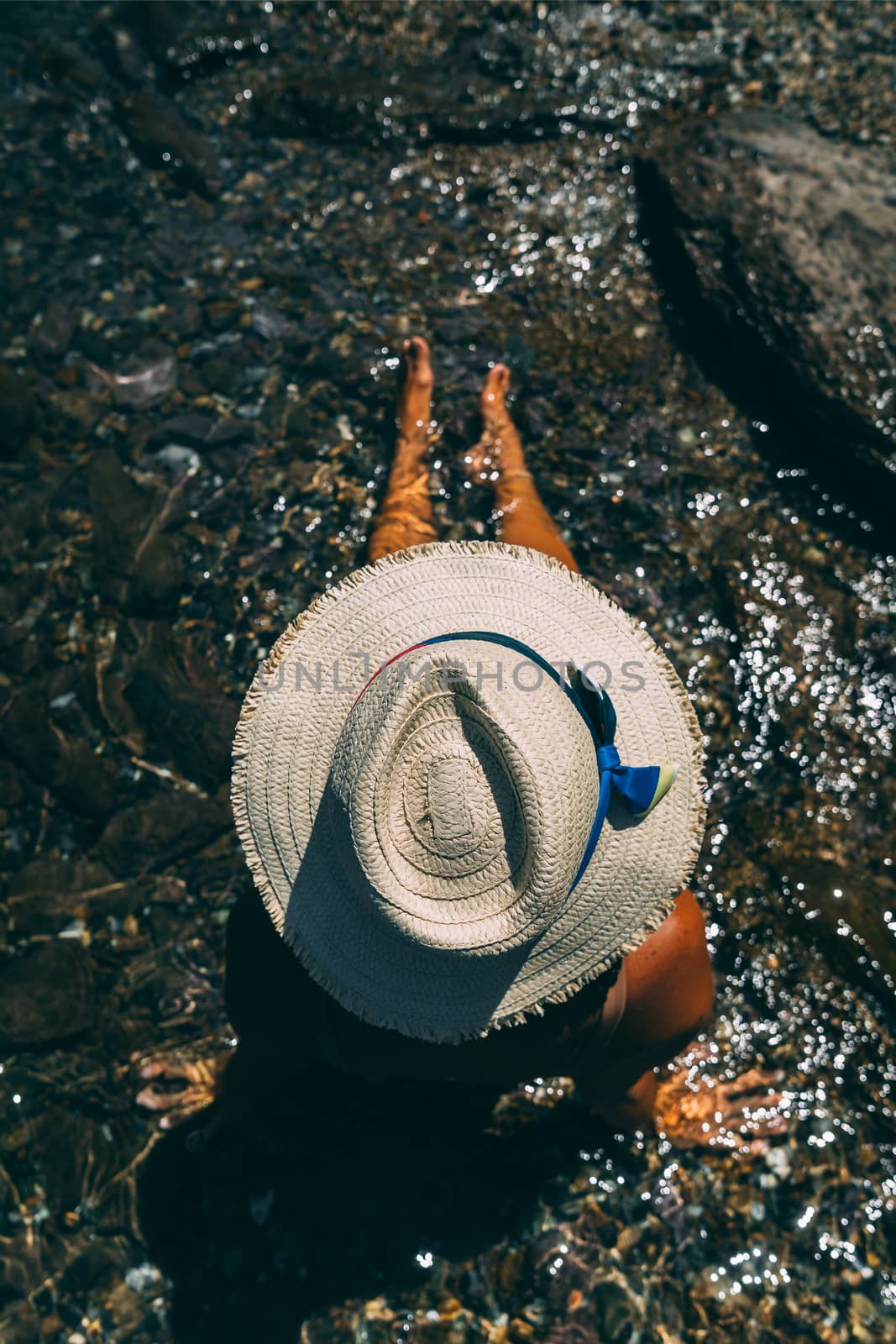 Young woman in white hat sitting in the water. by Emurado