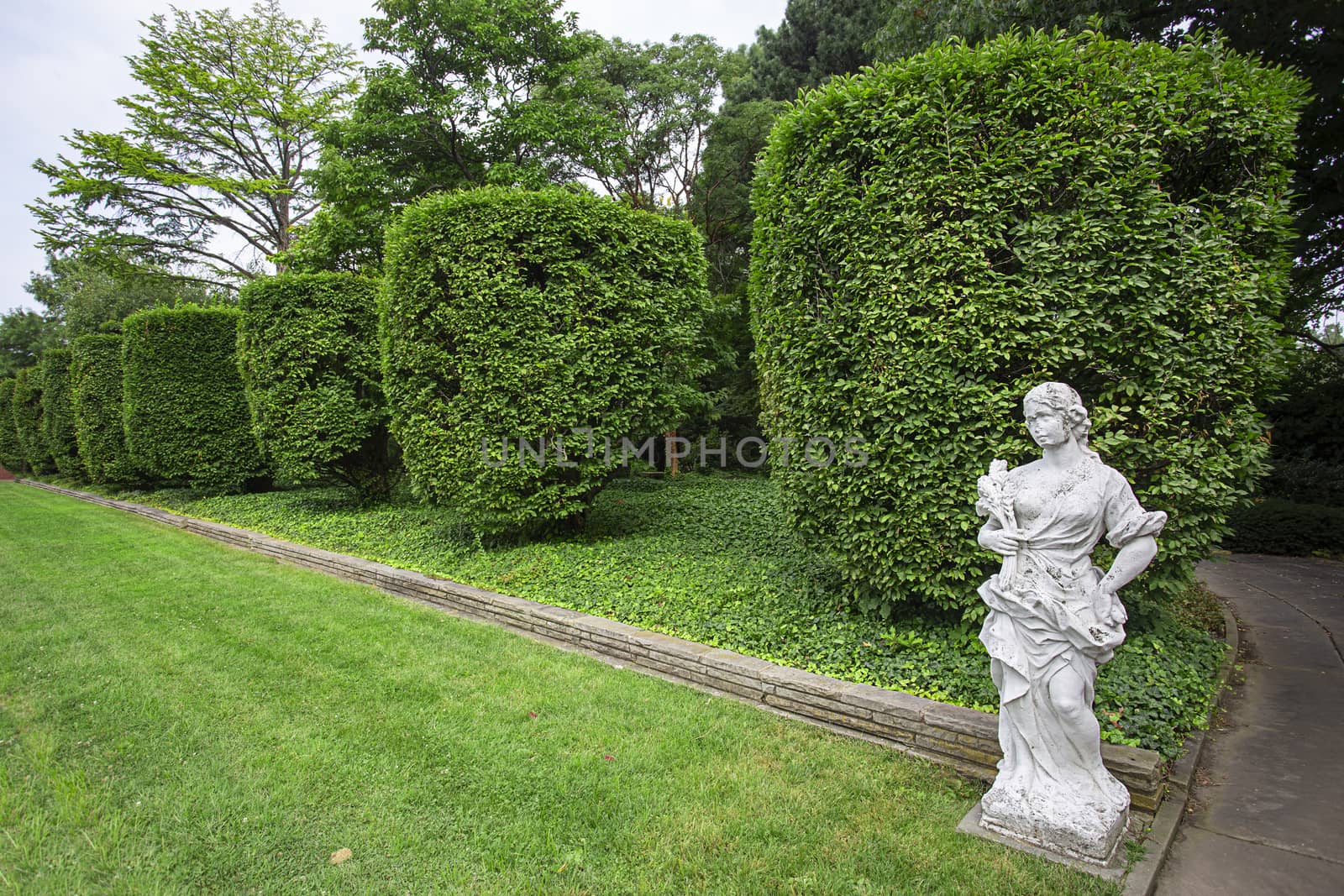 Formal garden with trimmed hedge and a marble statue of woman