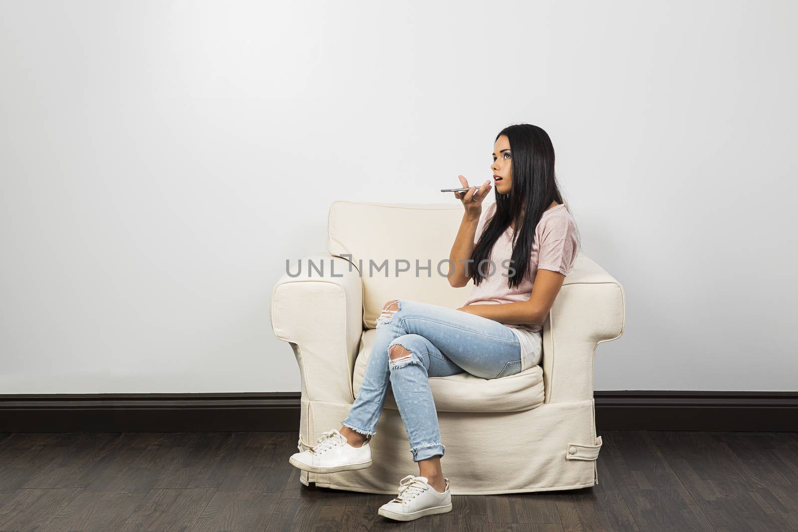 Young woman, sitting on a white couch, talking on her phone