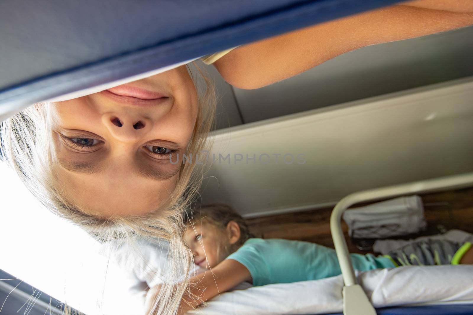 A girl hanging from the top shelf in a train looks into the frame