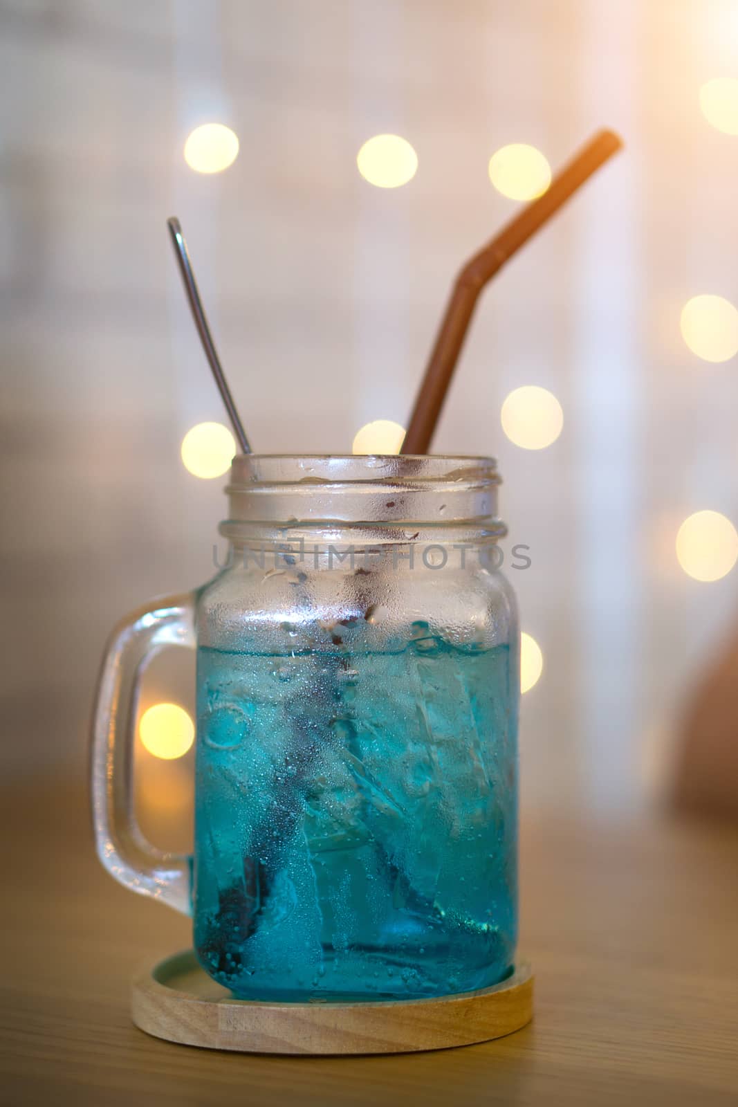 Cold blue cocktail drink, Blue Hawaii Italian Soda or sweetwater and yellow bokeh background in cafe.