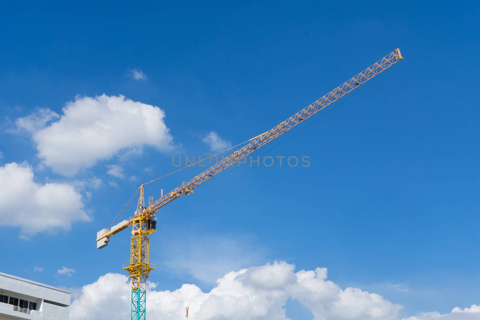 Yellow construction tower crane against blue sky.