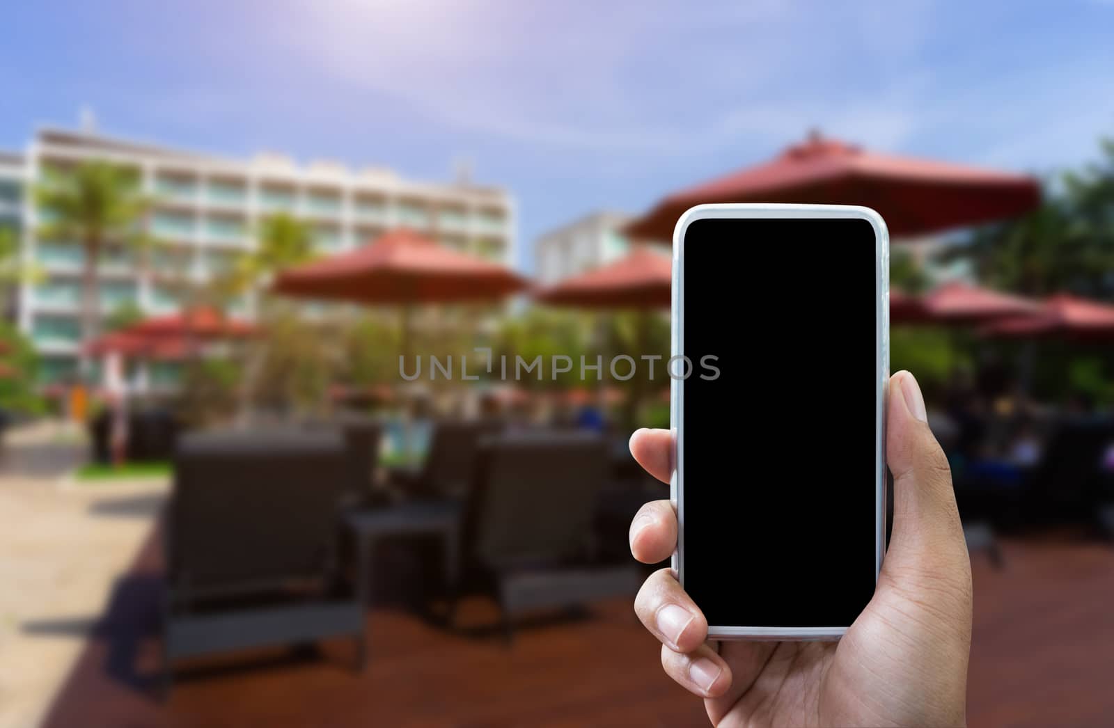 Man's hand shows mobile smartphone in vertical position mock up template and blurred hotel background for your Book hotel bussiness.