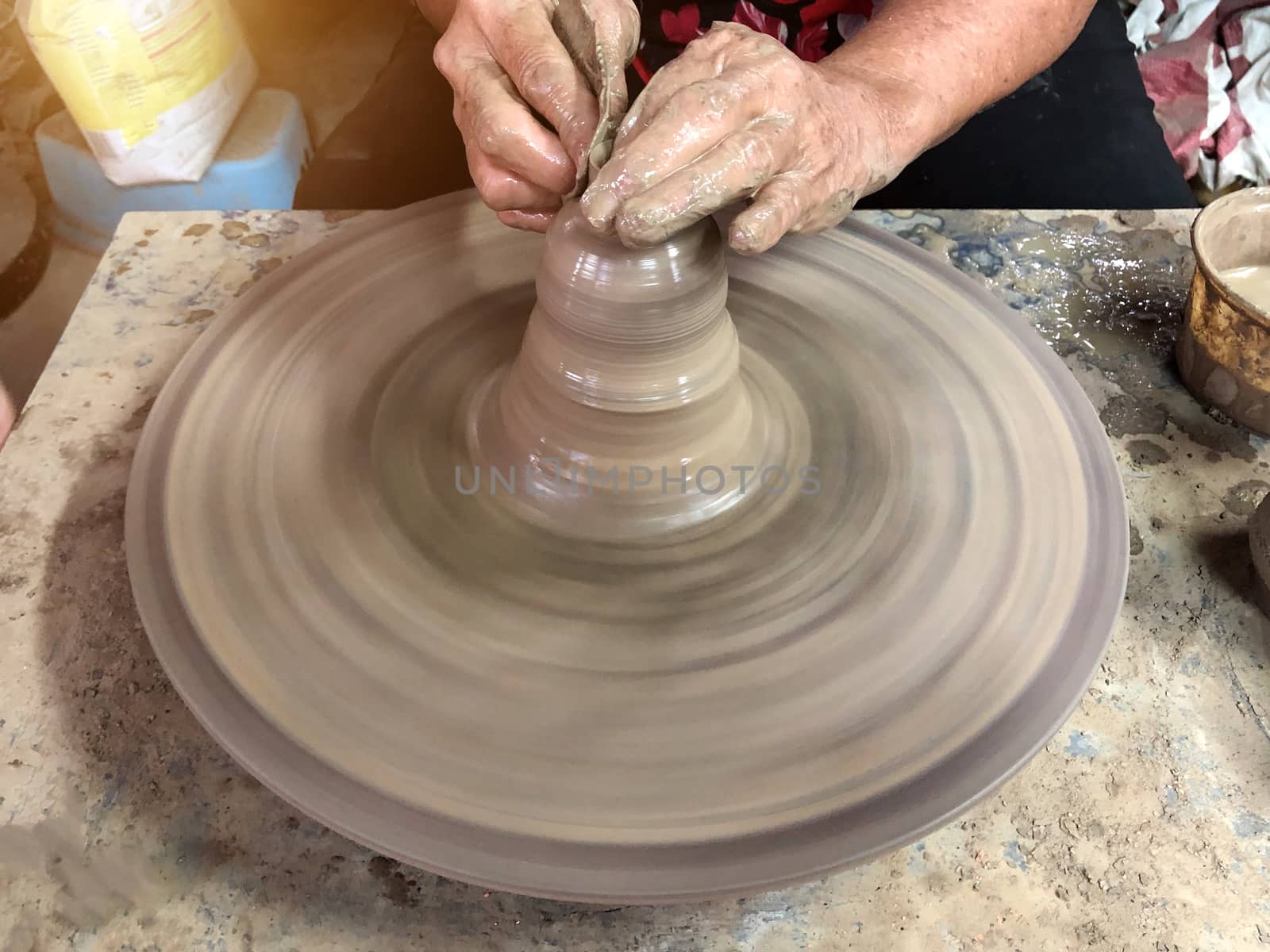 An older Asian woman Are making pottery by hand By placing it on the motor of the automatic rotating plate.