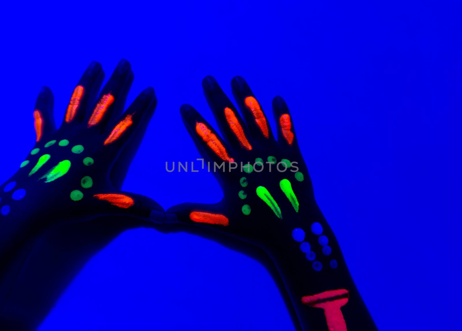 Close-Up Of Neon Painted Hand Against Blue Wall.